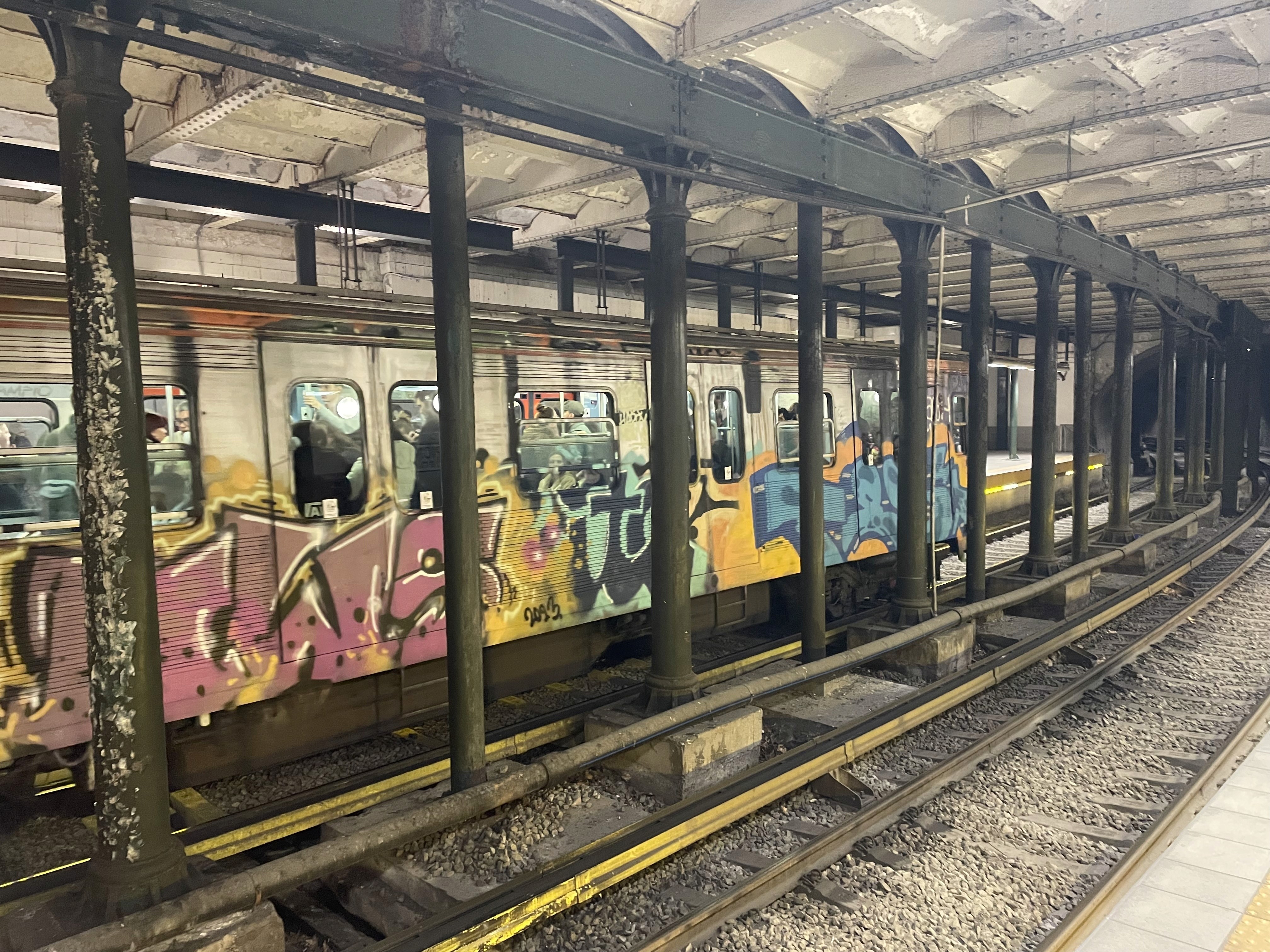 Vagone della metropolitana di Atene completamente ricoperto di graffiti colorati in una stazione storica con struttura metallica industriale