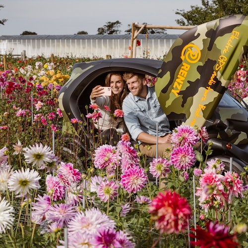 一对情侣在开着门的迷彩车中拍照，周围是一片色彩斑斓的花田。