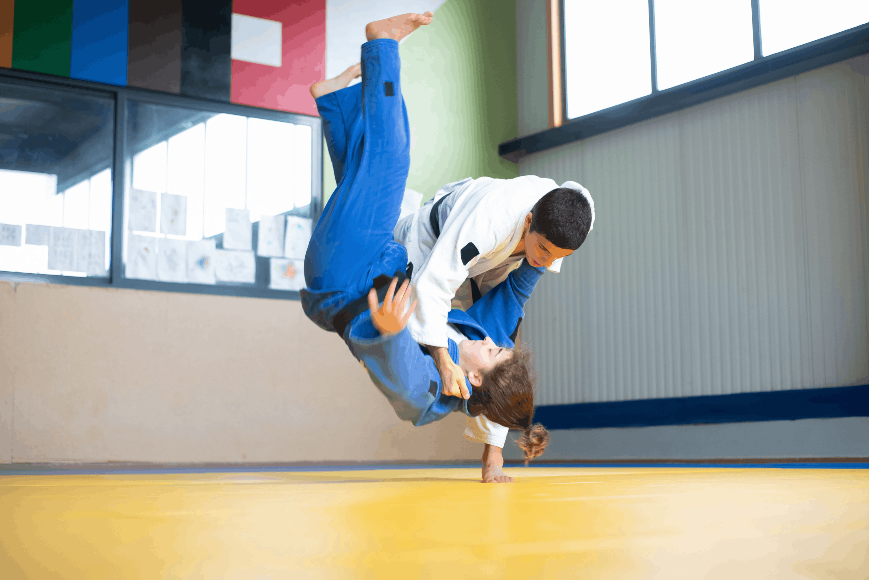 Two martial artists practicing a throw on a yellow mat