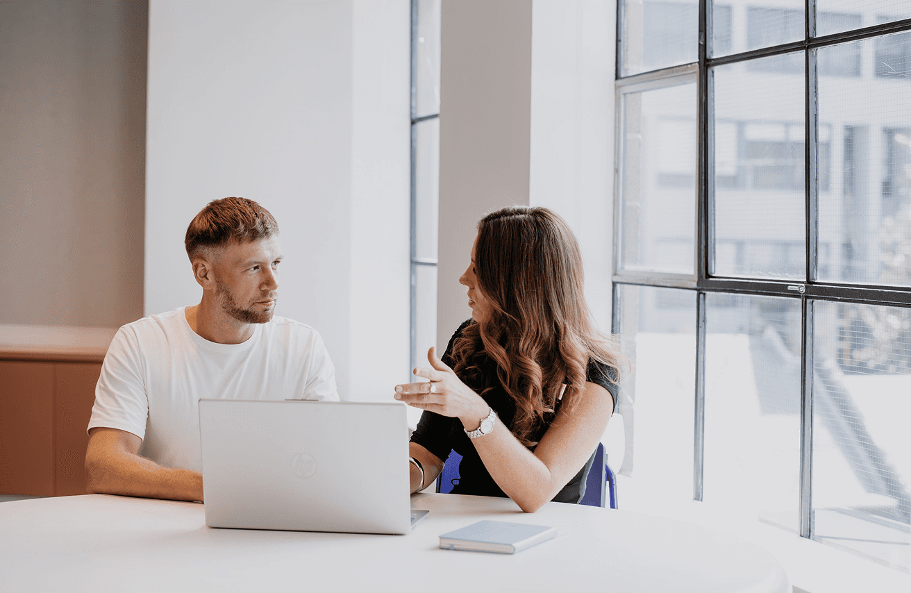 Two people talking at a table with a laptop.