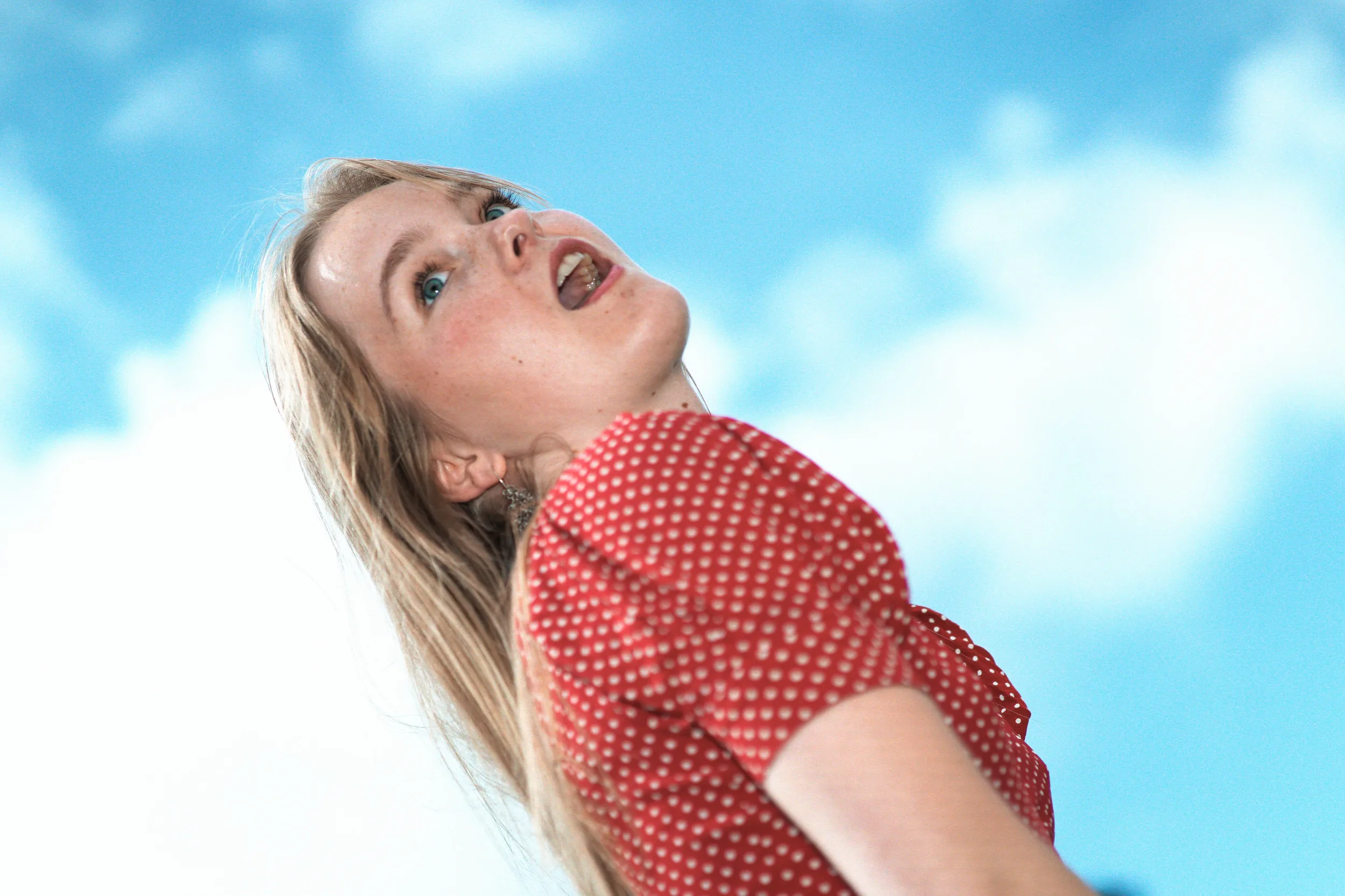 portrait pop d'une jeune femme blonde souriant devant le ciel dans sa robe rouge