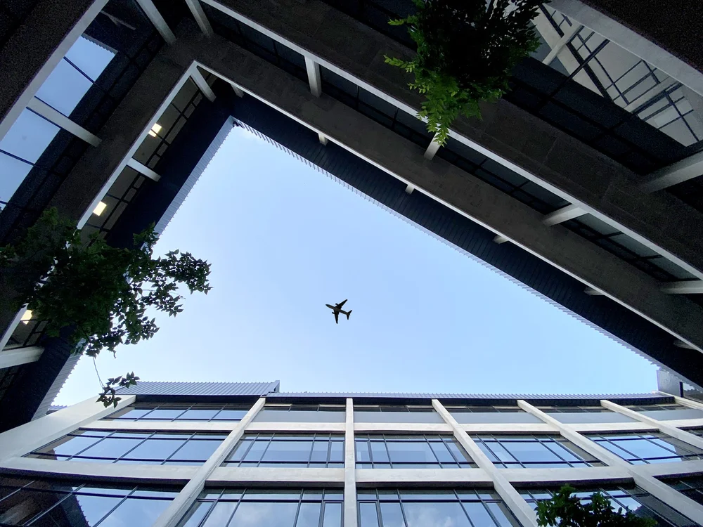 Modern luxury house with sharp angular roof, large glass walls, and pool and a city skyline at sunset.