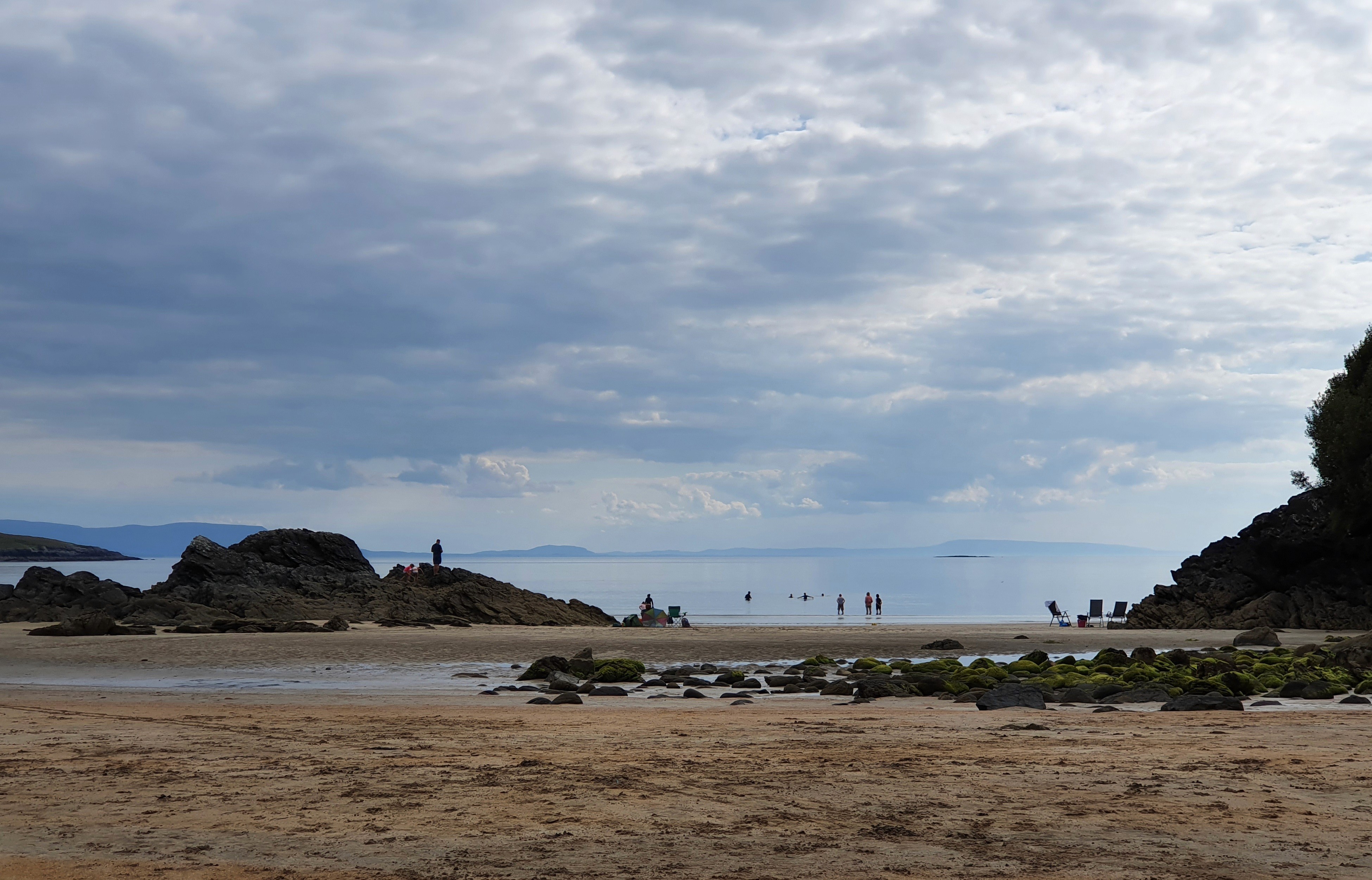 A scenic beach view with cloudy skies and distant hills along the coastline.