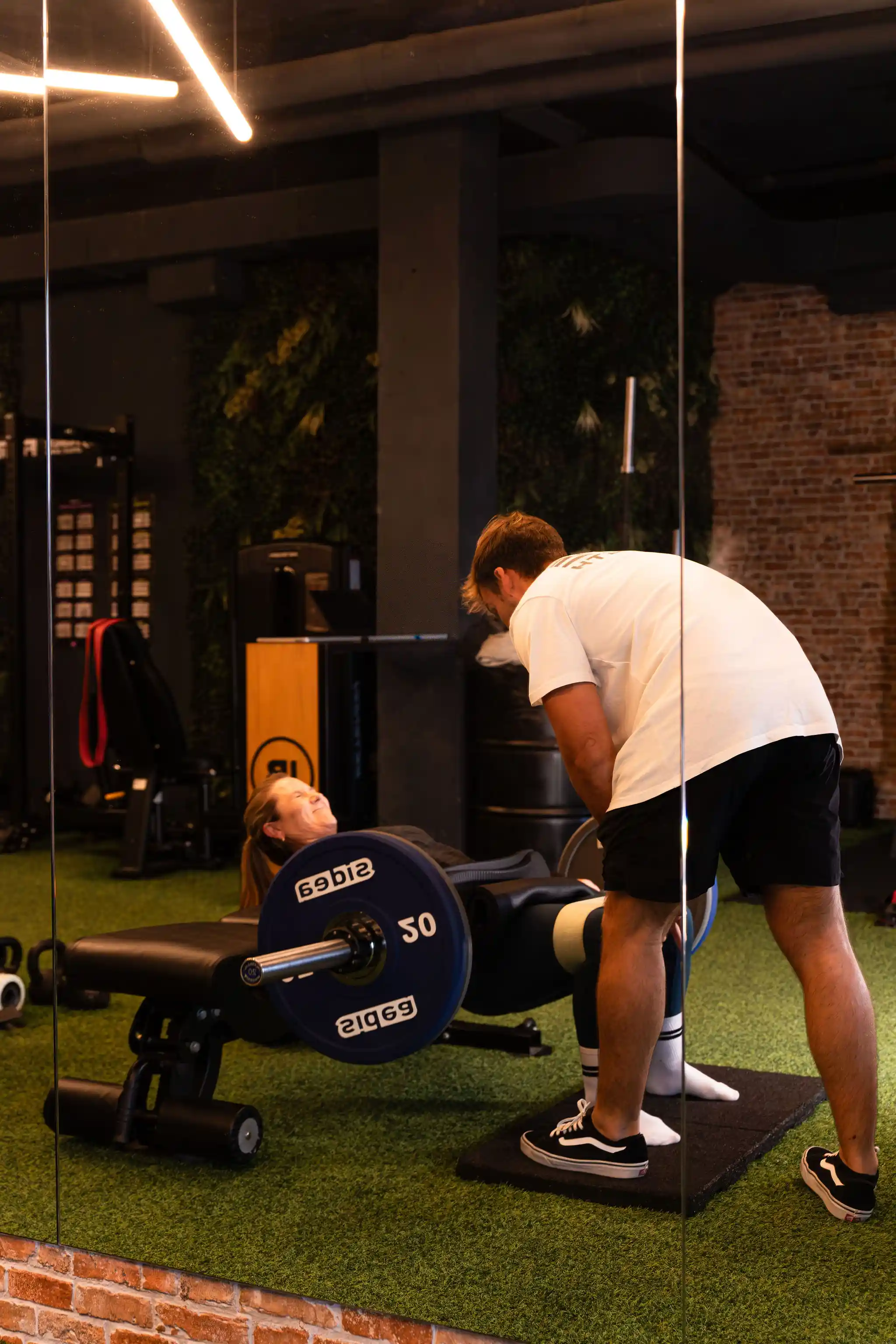 Entrenador corrigiendo técnica de empuje de cadera a clienta en La Base Strength, Sitges