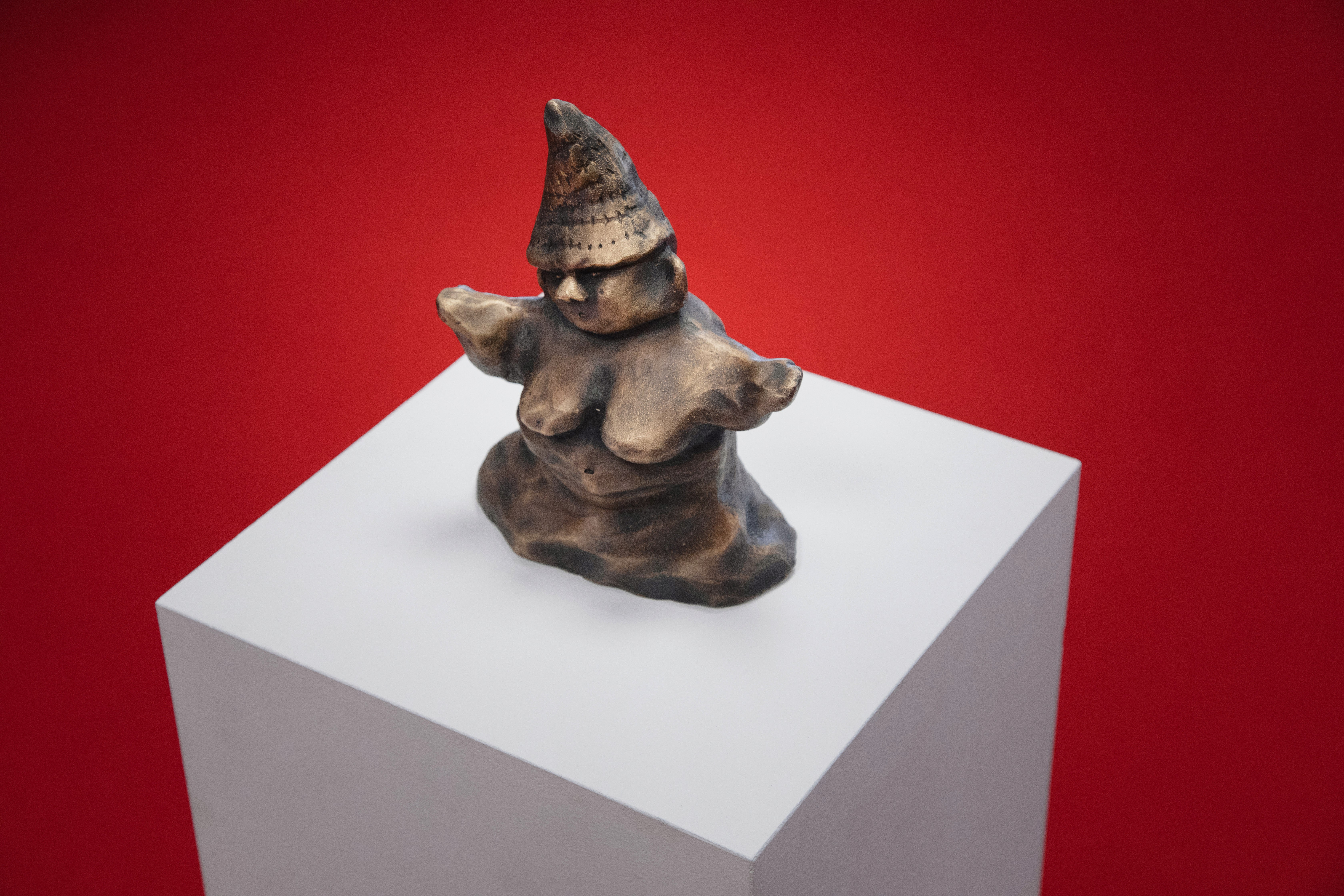 Venus Gnome, a small bronze sculpture by Ásta Fanney Sigurðardóttir, on a white plinth against a red background.