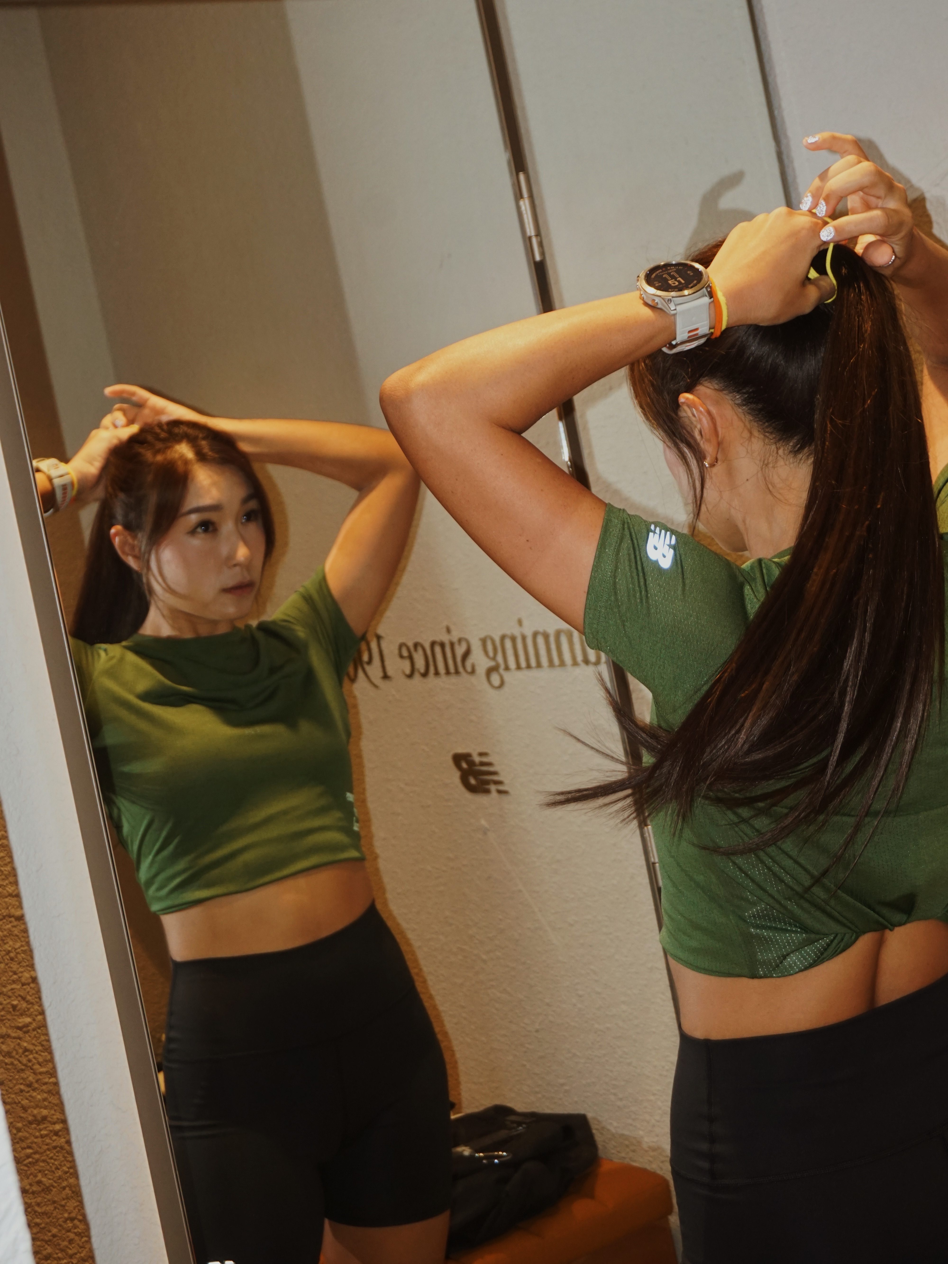 Yen tying her hair in front of a mirror, preparing for a run. She appears focused and ready to start her workout.