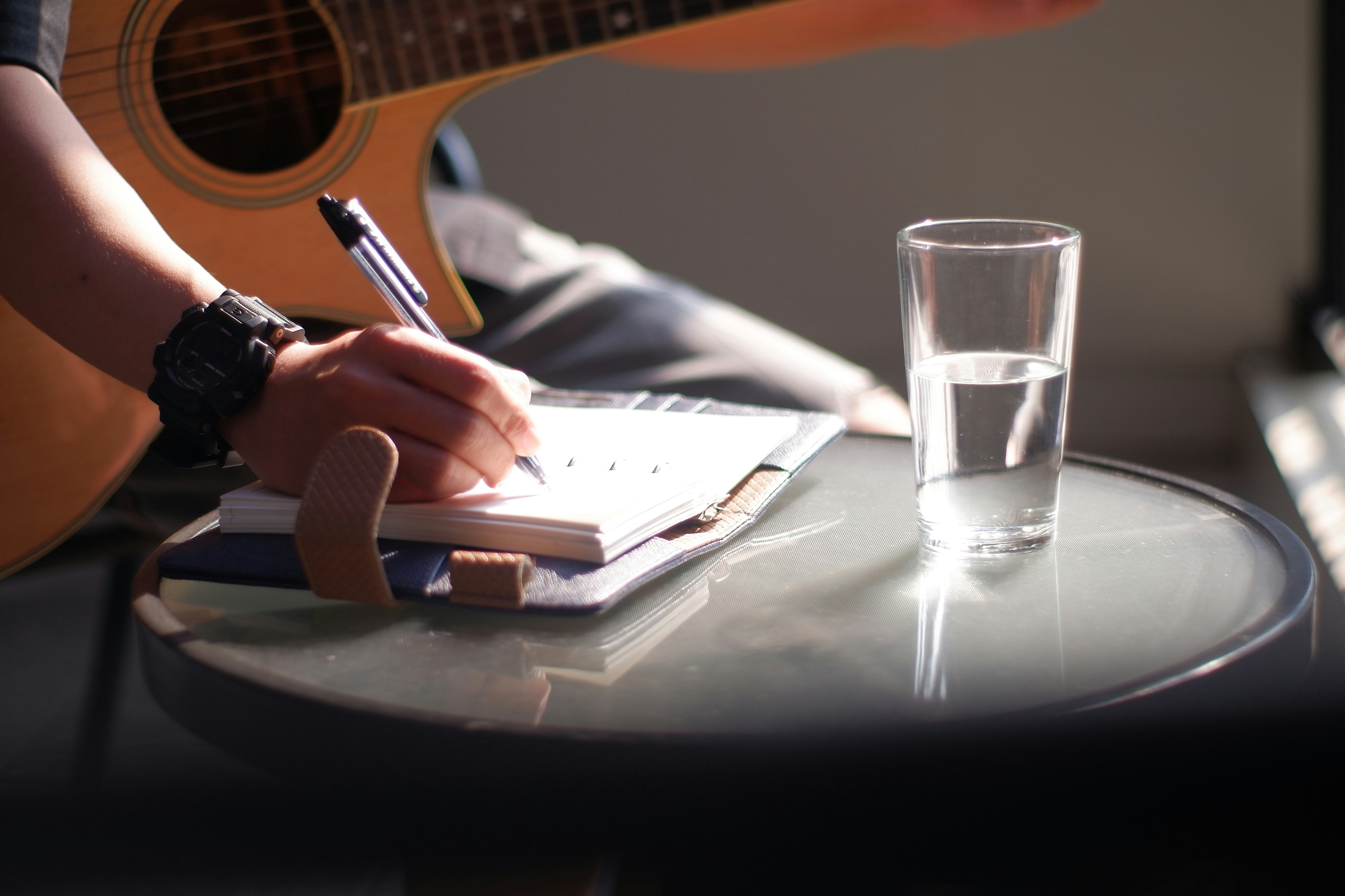 A musician with a guitar songwriting lyrics into a notebook. Photo by Adhy Setya on Unsplash
