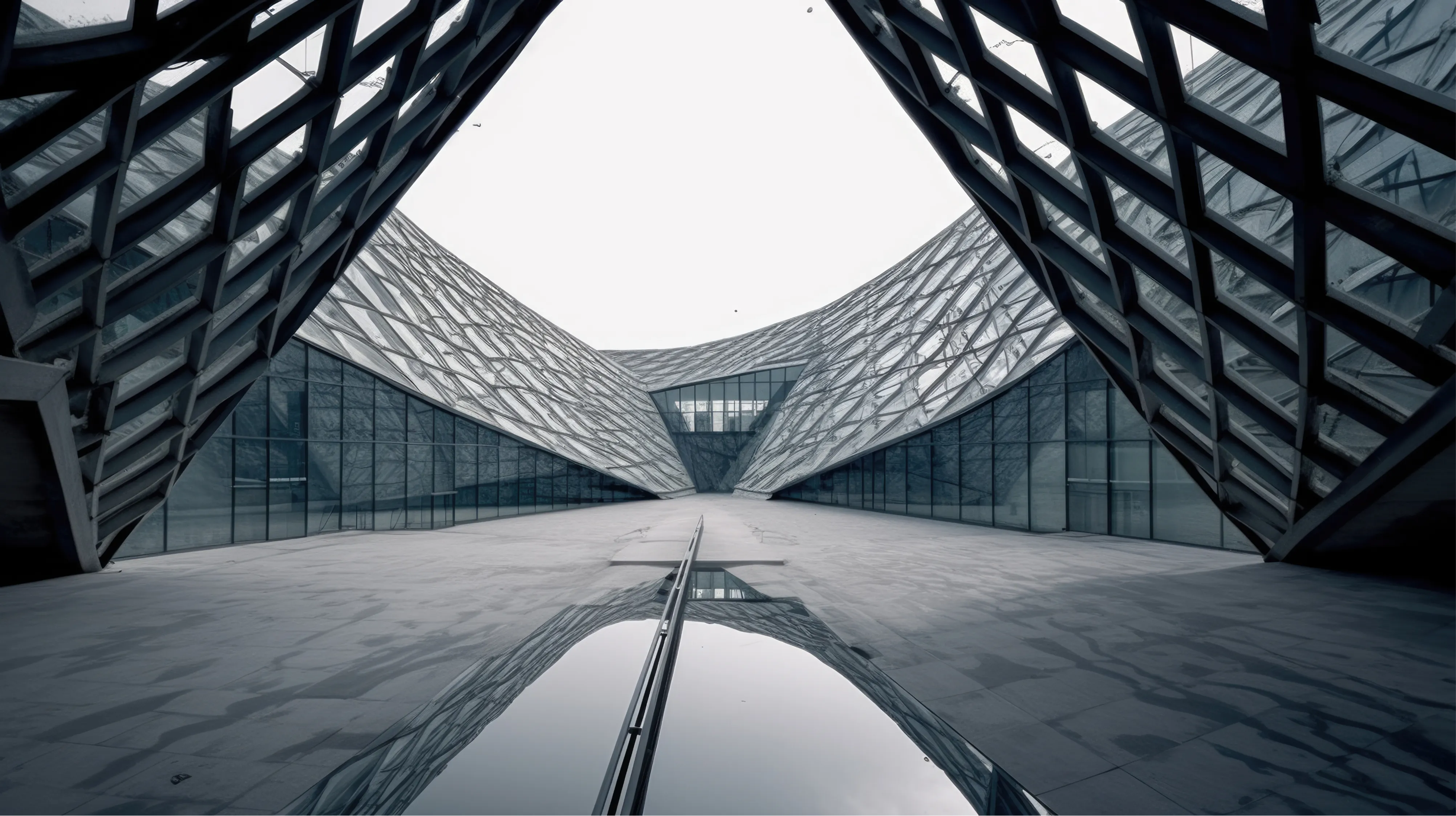 A wide-angle, low-perspective shot of a modern architectural structure featuring a vast, open courtyard paved with dark, reflective stone. The building is characterized by a complex, interlocking diamond-patterned steel or glass lattice that curves upward toward a bright, overcast sky. A small pool of water on the ground creates a crisp reflection of the geometric roofline.