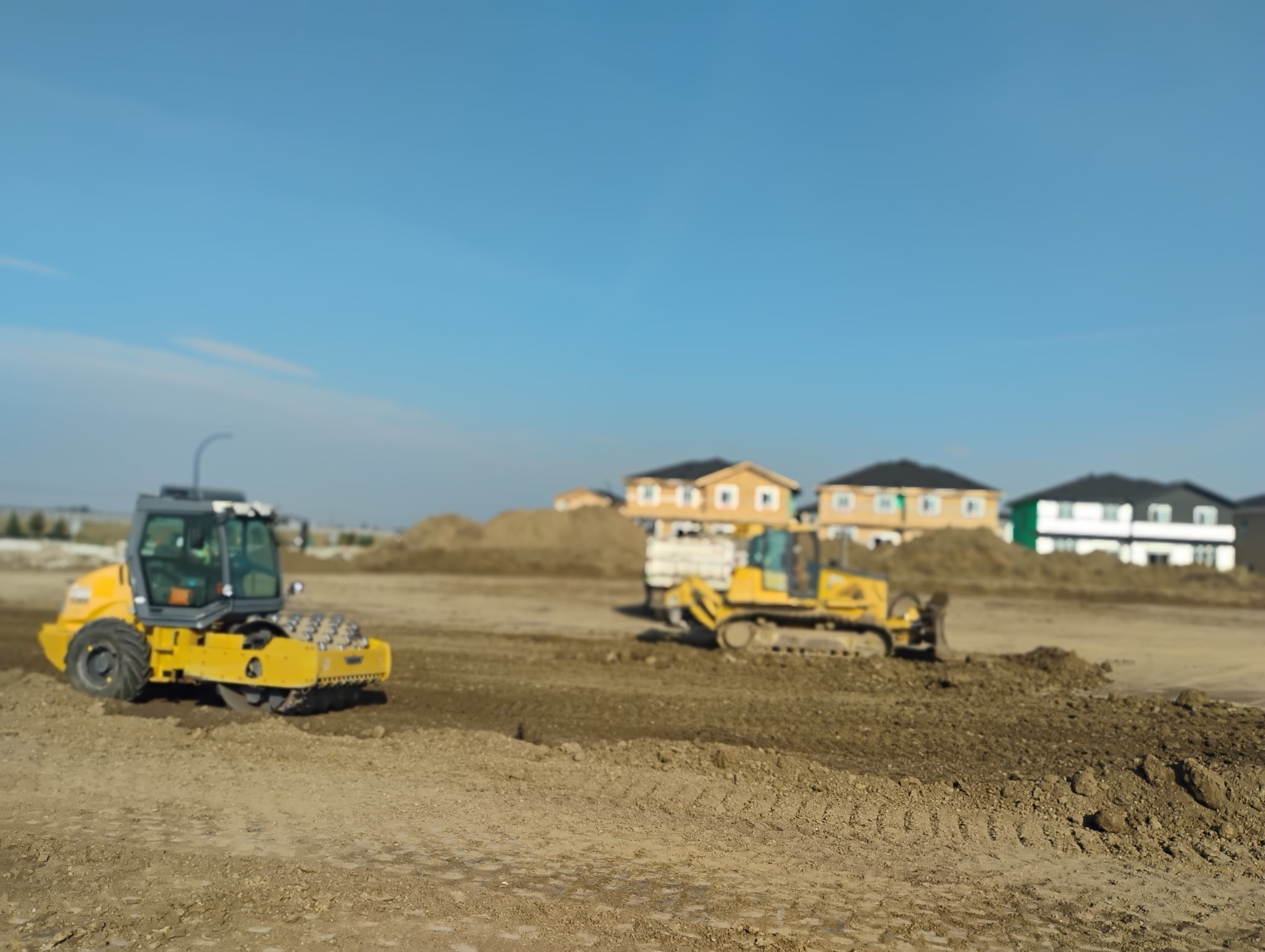 a dozer pushing dirt while a packer compacts it
