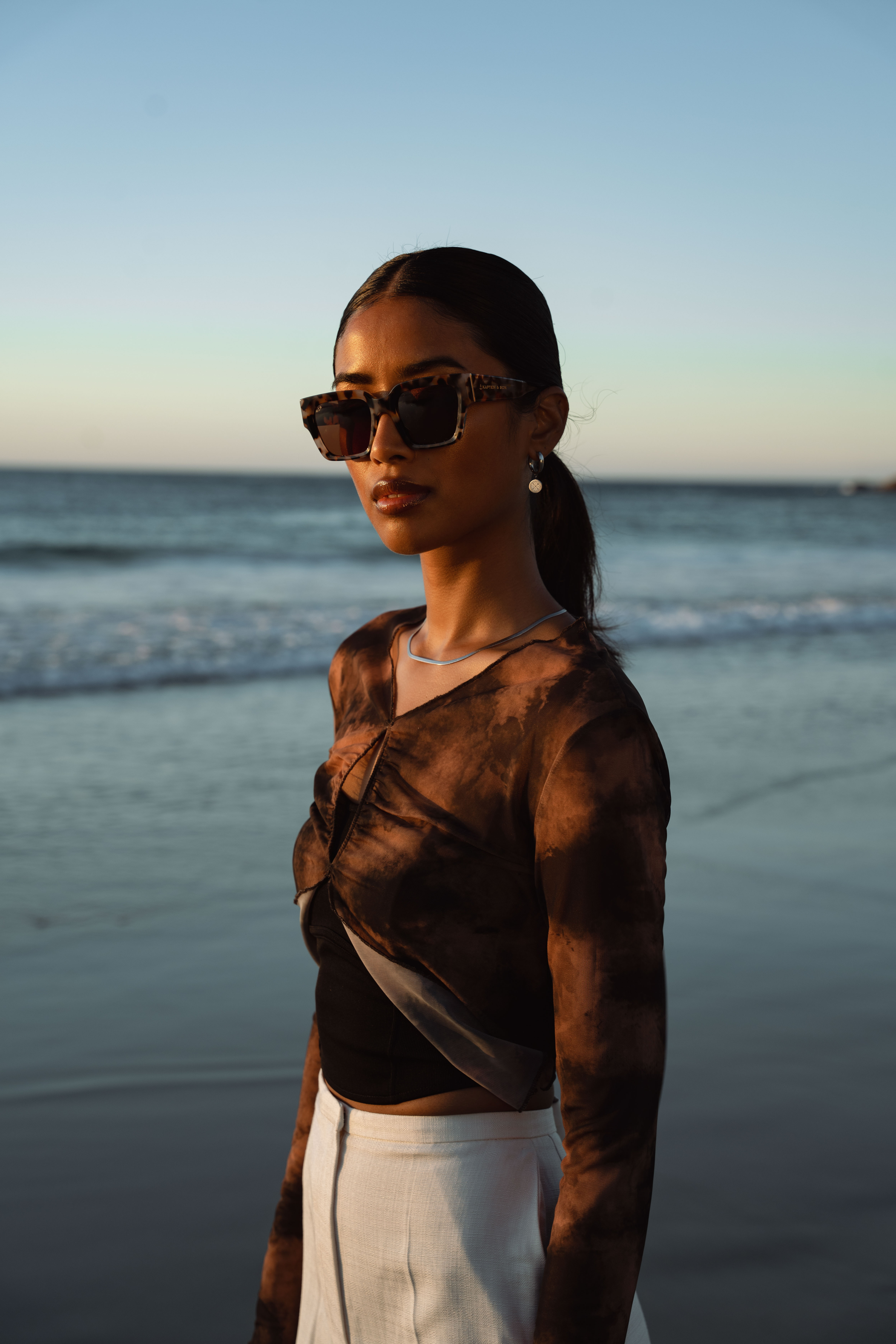 Une femme porte des lunettes de soleil devant la mer dans le lookbook de la marque Kapten
