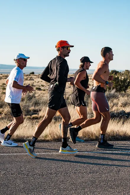Four runners jogging together along a desert road.