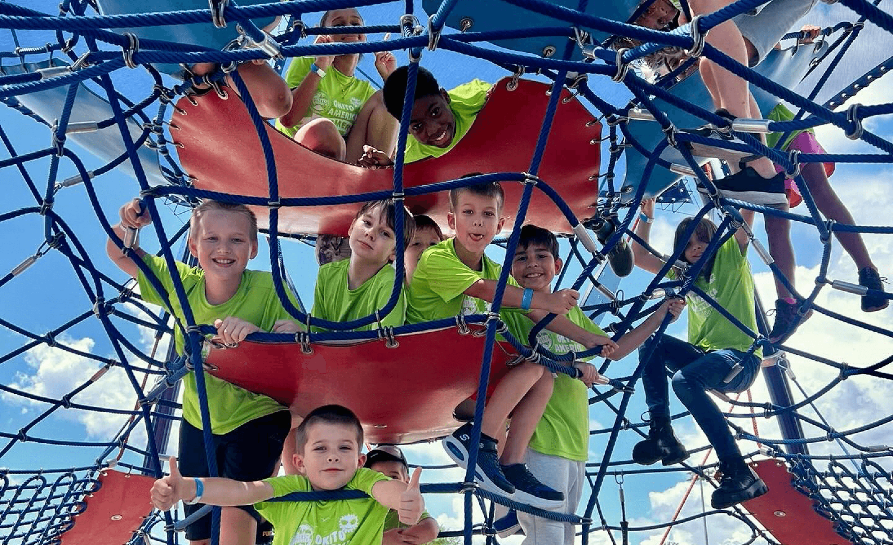 Group of kids hanging on a jungle gym at a camp outing smiling at the camera.