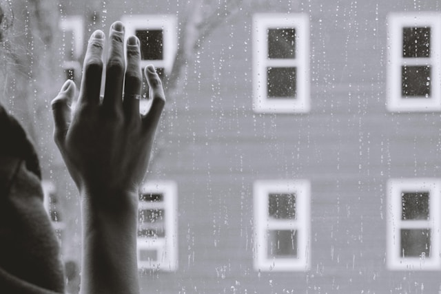 woman's hand on raindrop covered window