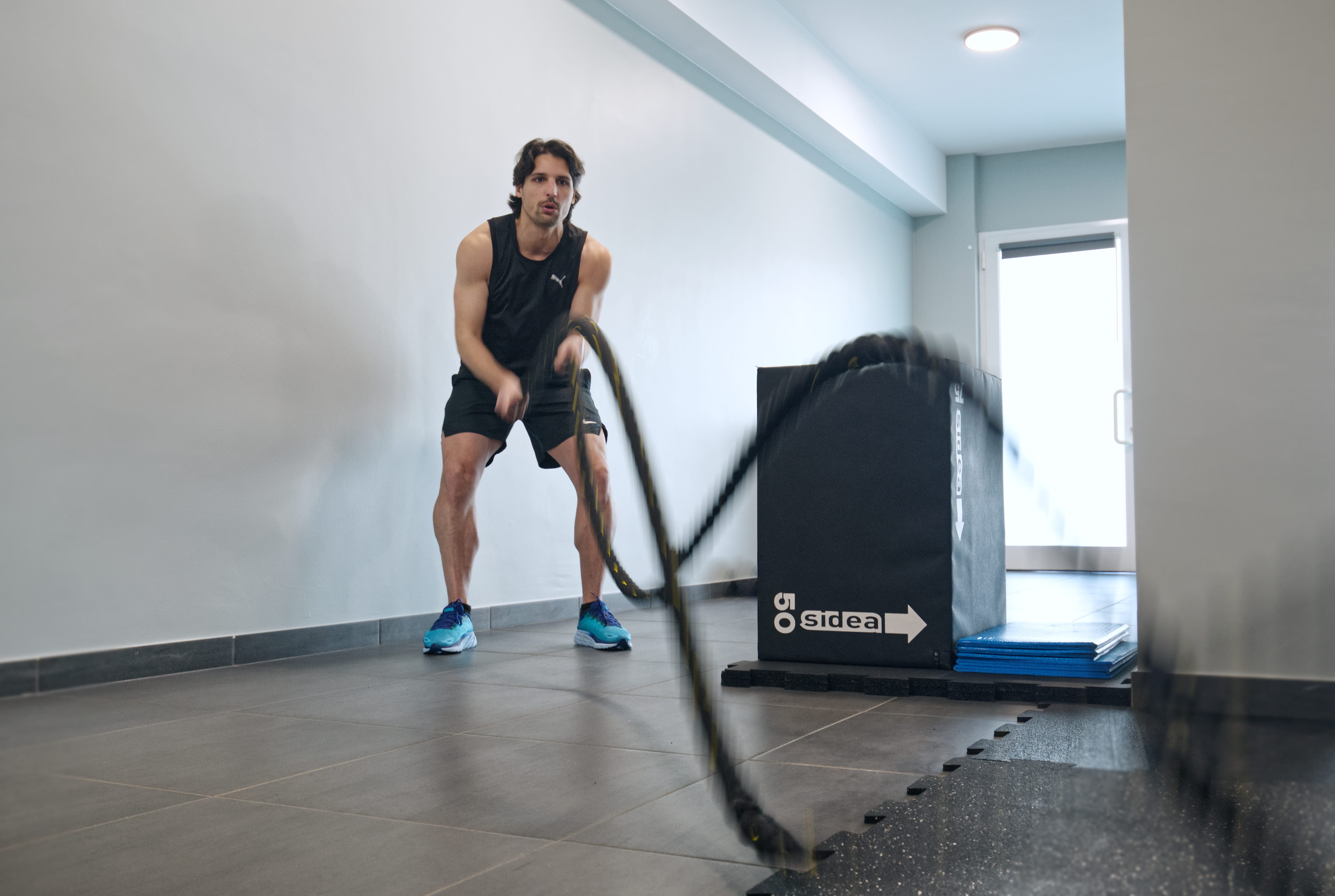 A person in a white outfit sits on a round stool in a spacious, minimalist room. The wall is covered with framed photos surrounding a large screen, creating a serene, contemplative atmosphere