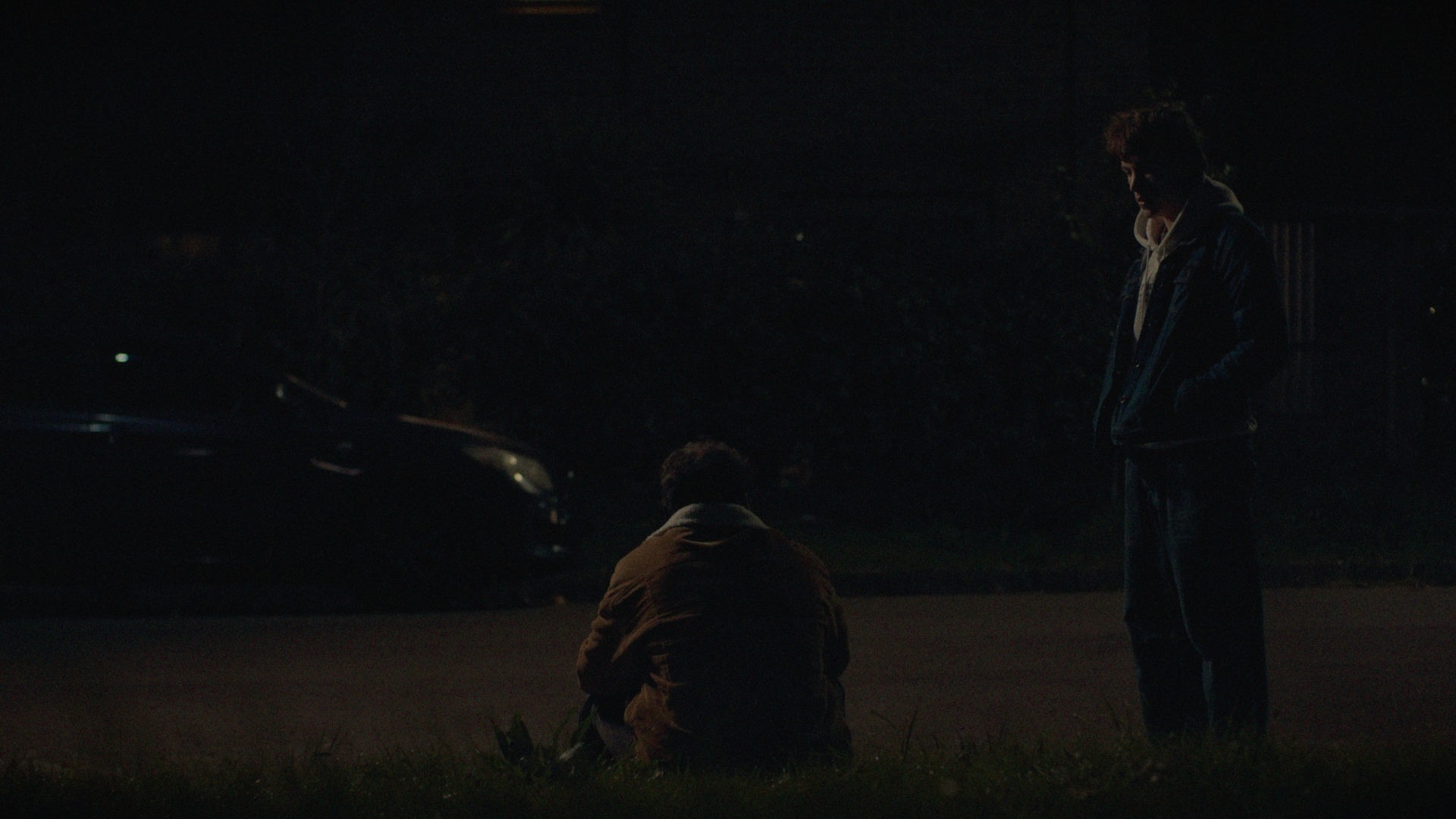 Two guys hand by the side of a curb at night