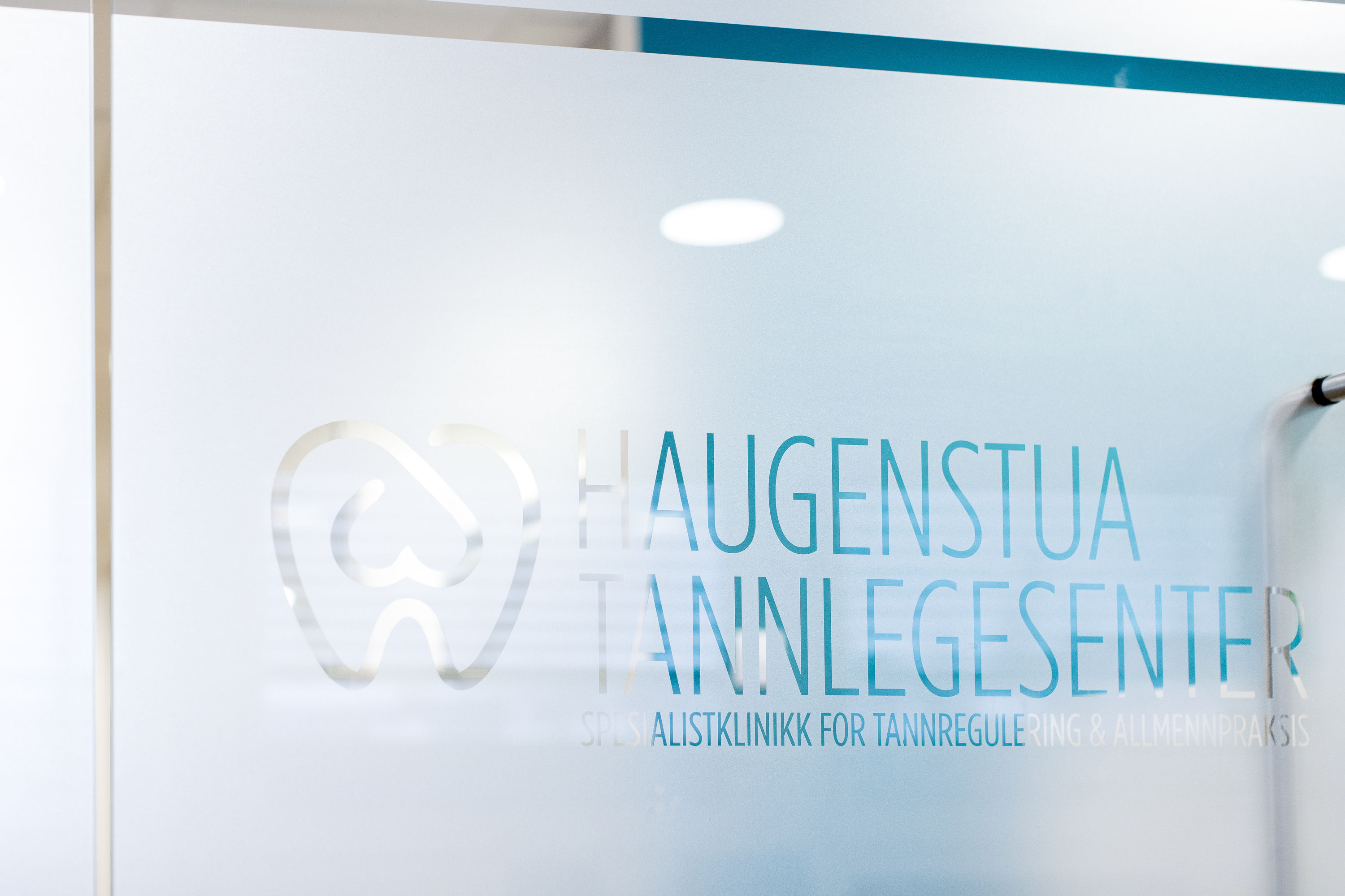Nærbilde av inngangsdør med logoen til Haugenstua Tannlegesenter, som viser klinikkens moderne og profesjonelle profil.