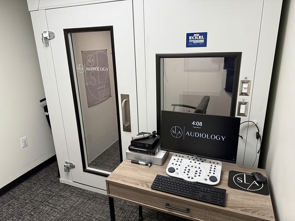 A room with a soundproof booth, a computer desk, and equipment for audio recording or testing.