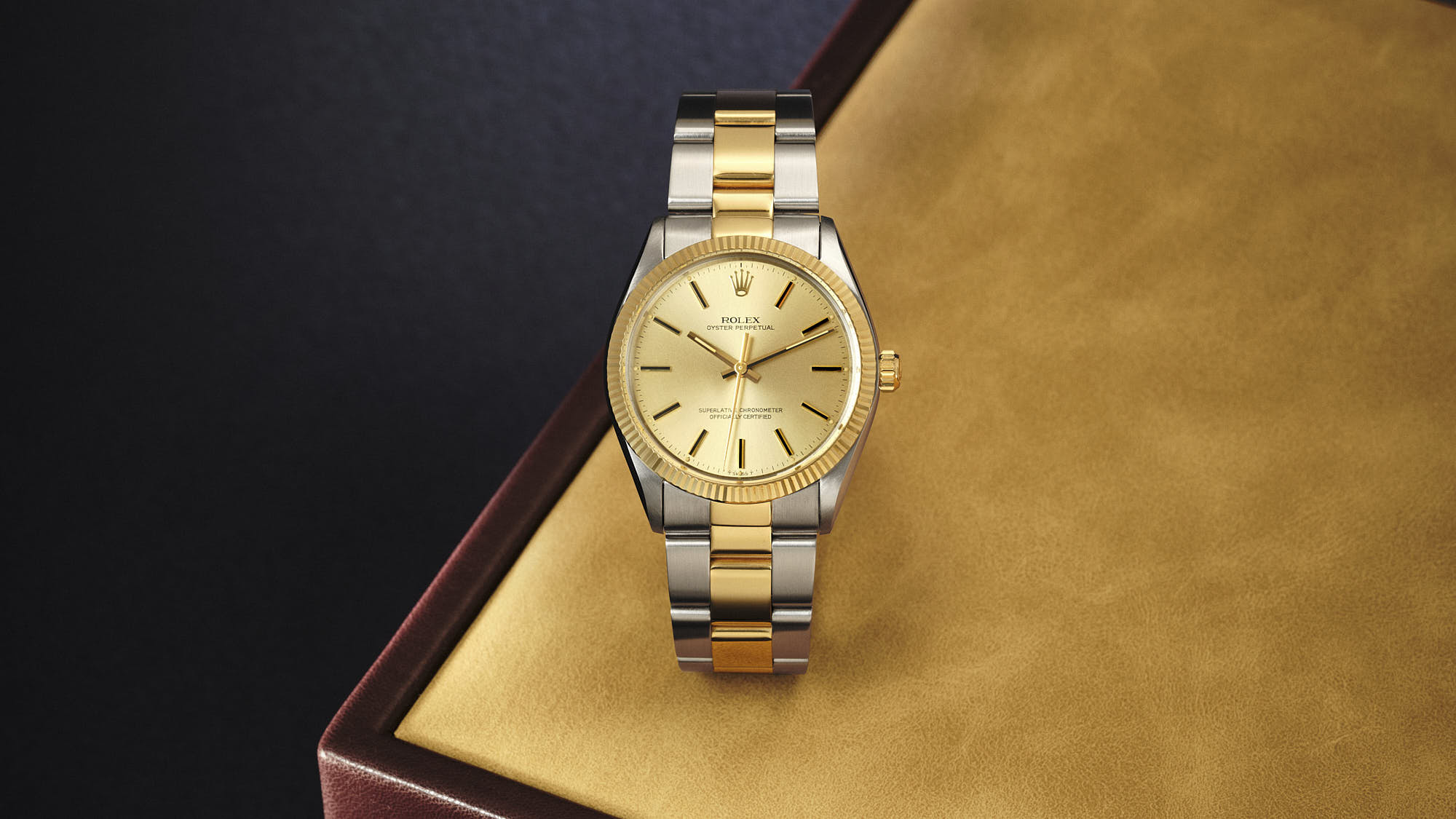 Luxury Rolex Oyster Perpetual watch with gold dial and two-tone bracelet on leather surface.