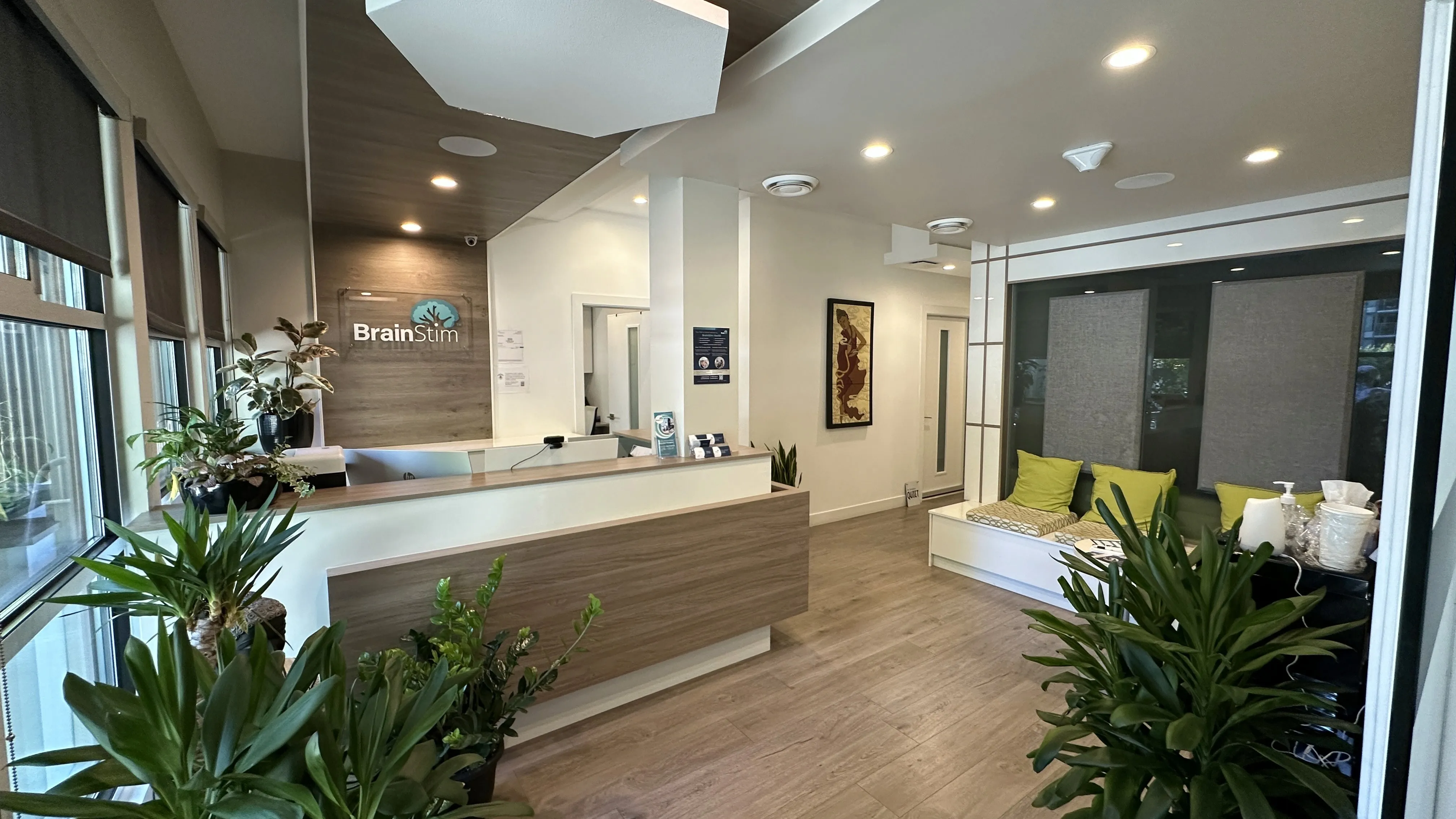 BrainStim Vancouver reception desk with signage, potted plants, and a lounge bench with green cushions