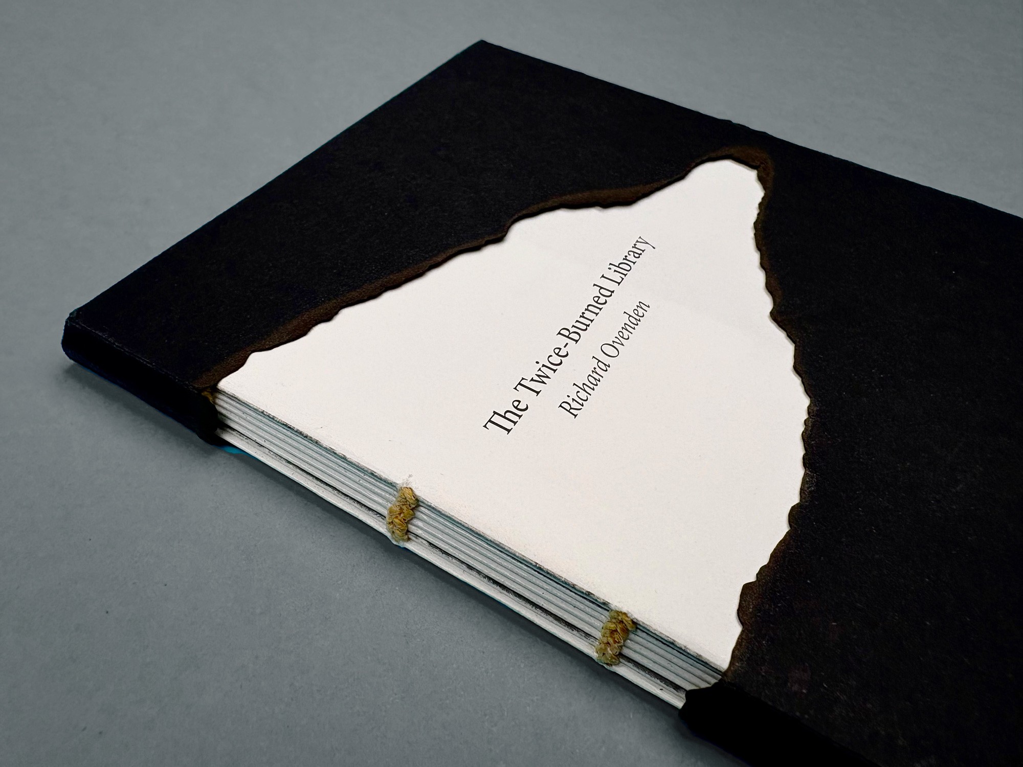 Een schuin bovenaanzicht van het boek. De cover heeft duidelijk afgebrande randen en de fragiele bindingen zijn zichtbaar, wat het kwetsbare karakter van de inhoud weerspiegelt.