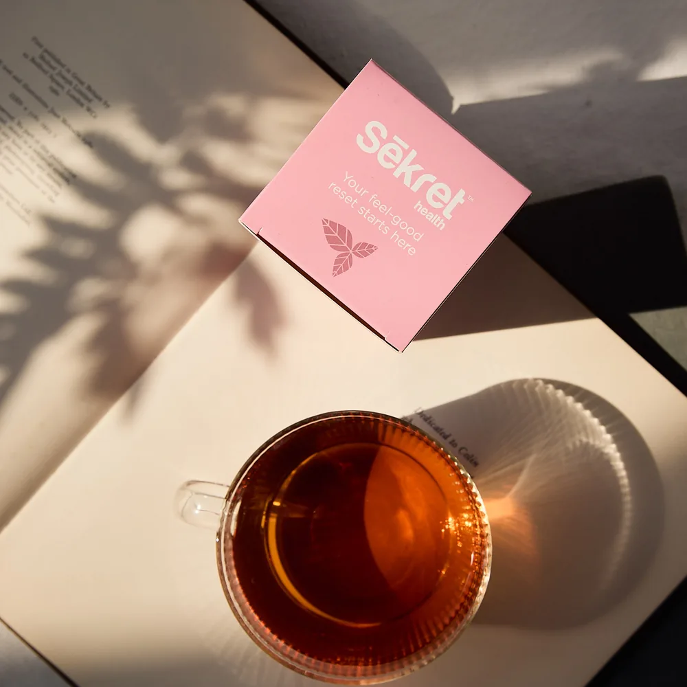 A cup of Sekret herbal tea beside its box in afternoon light