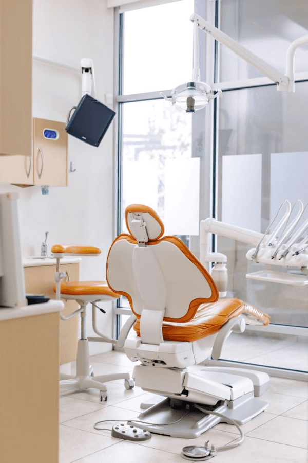 Dental exam room with an orange patient chair and overhead light.