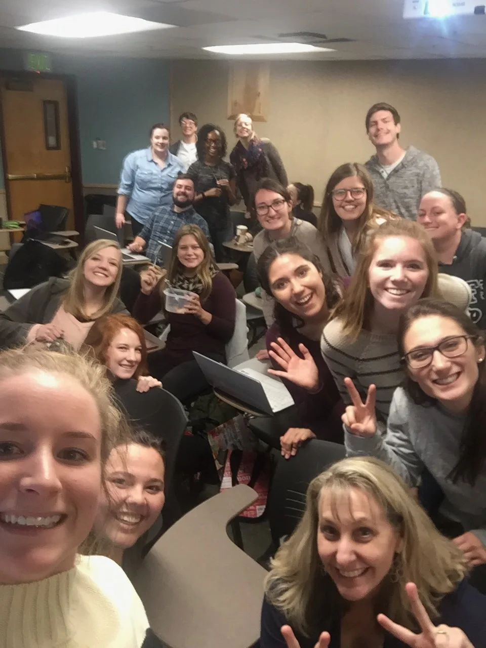 A large group of people smiling and posing for a selfie in a casual indoor setting.