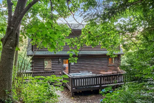 Log cabin with a deck and hot tub in the woods