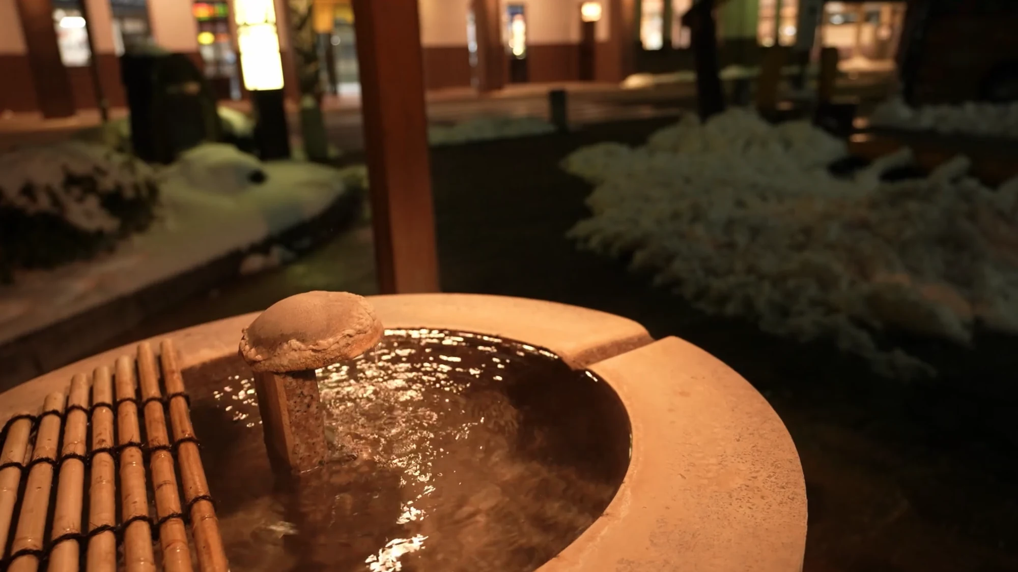 A snow-rimmed stone drinking basin steaming gently under lamplight in Kinosaki.