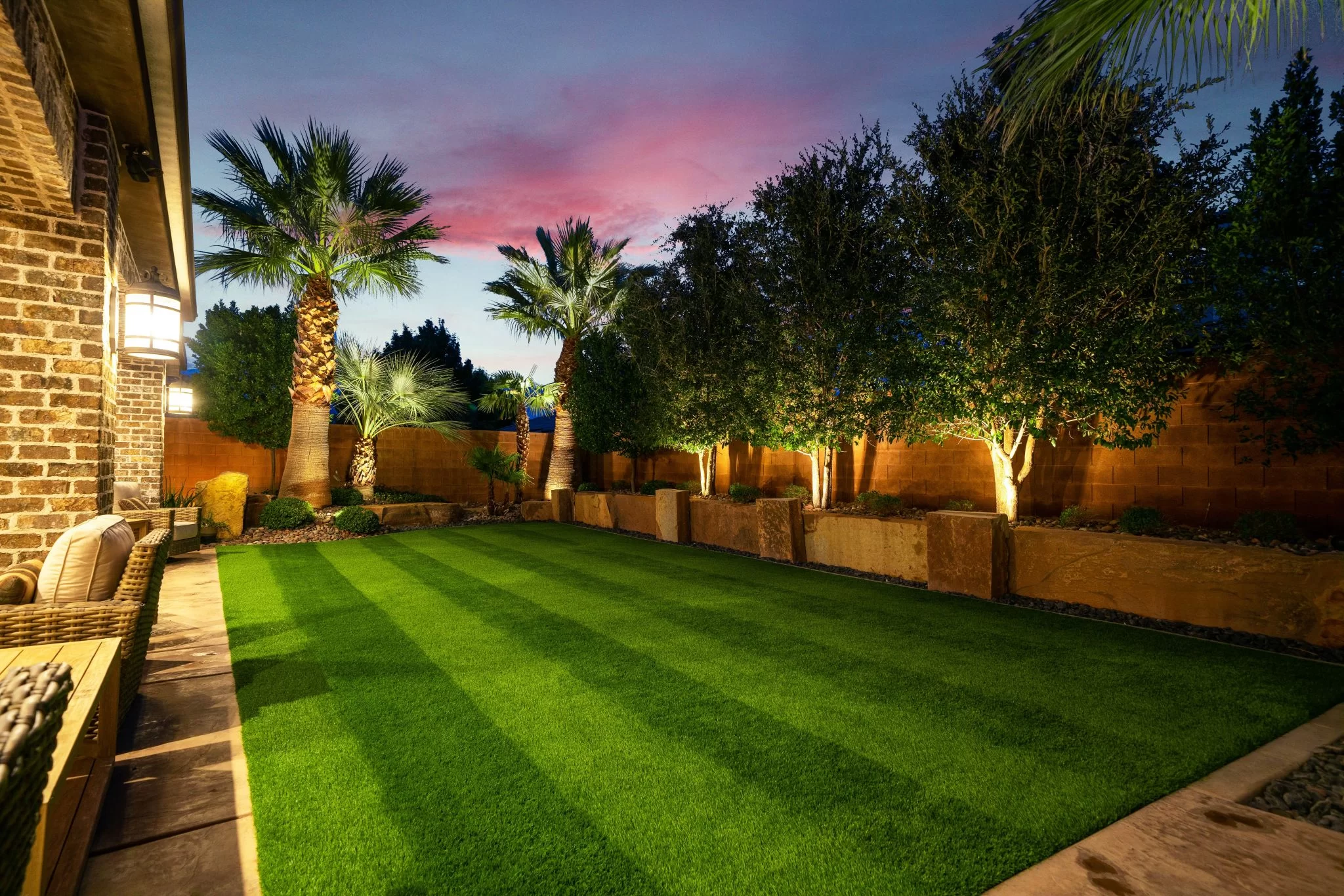 This is a picture of an inviting backyard at sunset adorned with lush artificial AGL Grass and softly glowing lights, creating a cozy ambiance.