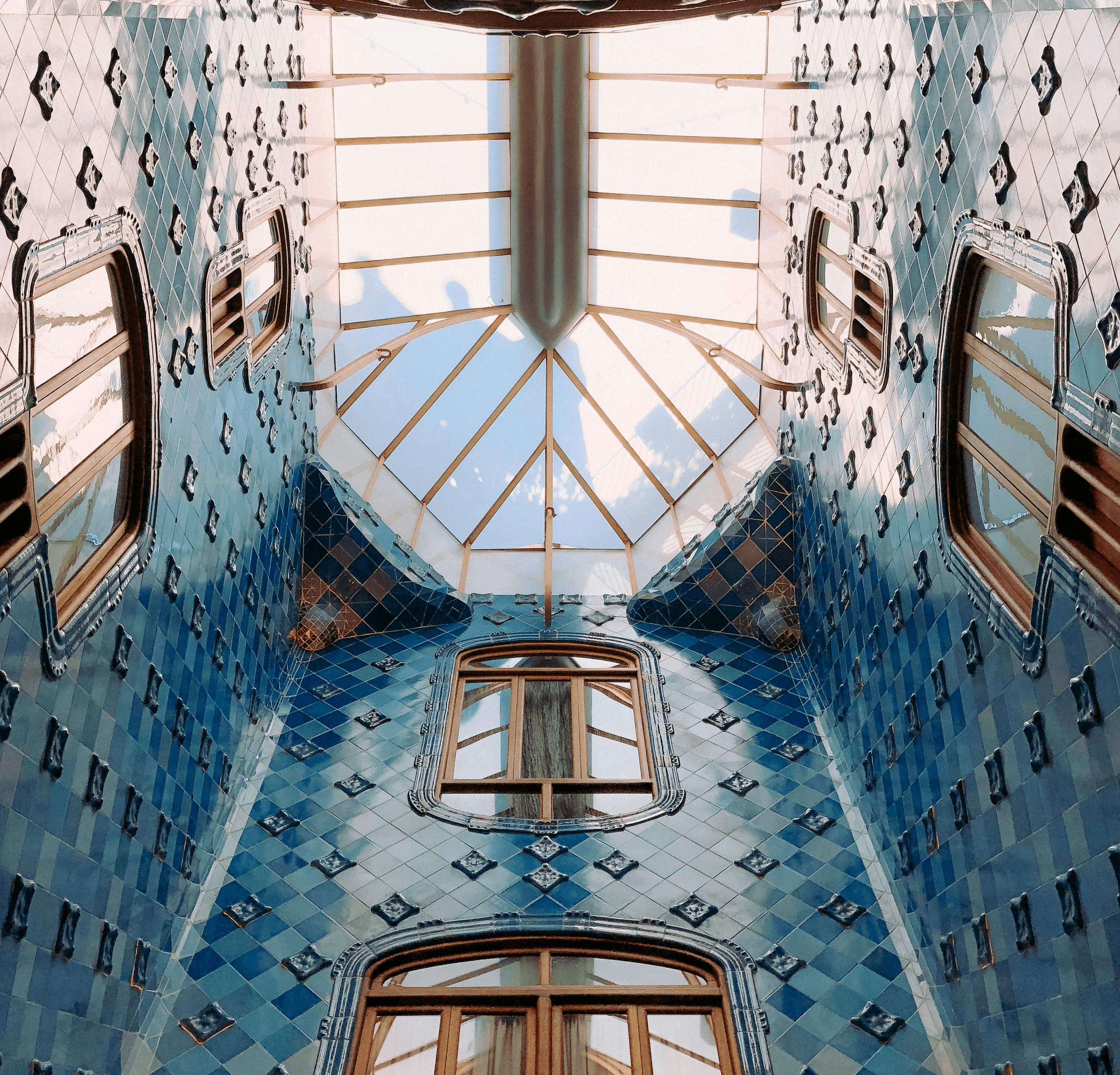 Light pours through a skylight into an airy atrium lined with blue tiles and windows in Casa Batllo.