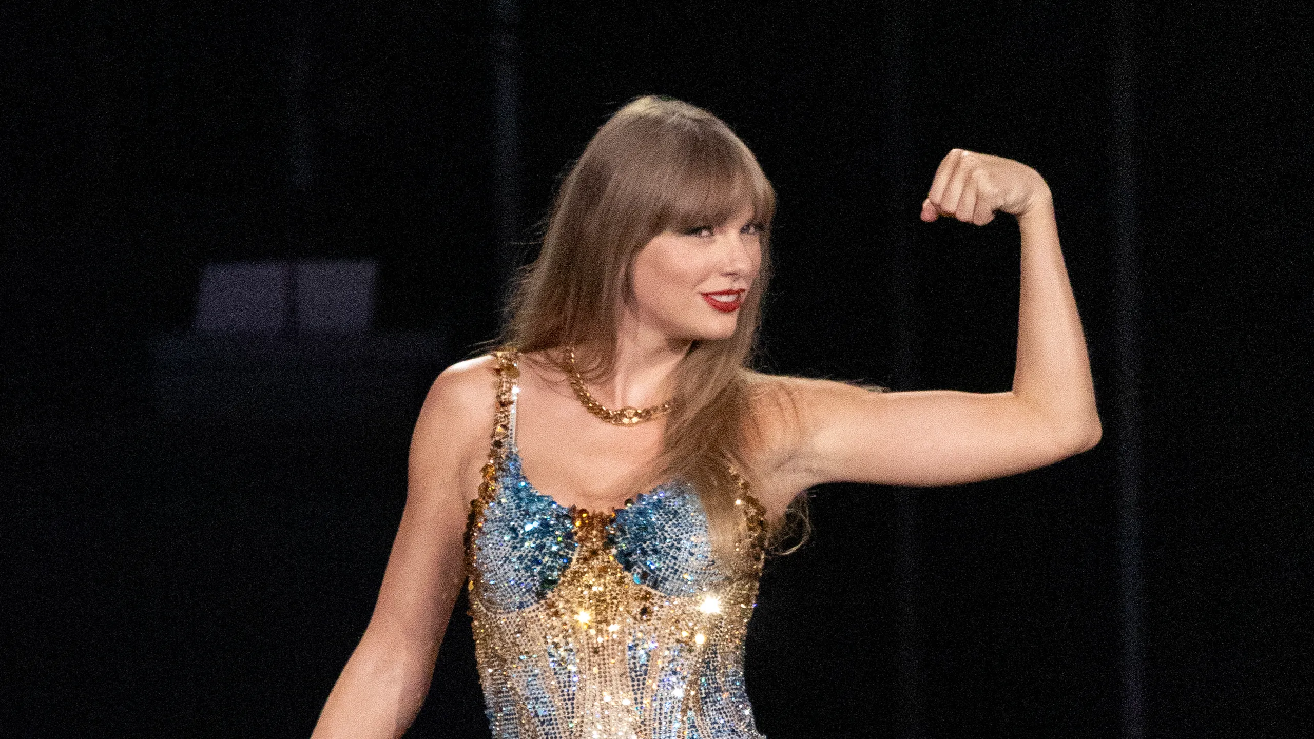 Taylor Swift posando y haciendo el gesto de fuerza con el brazo, vestida con un vestido de lentejuelas durante su gira The Eras Tour.