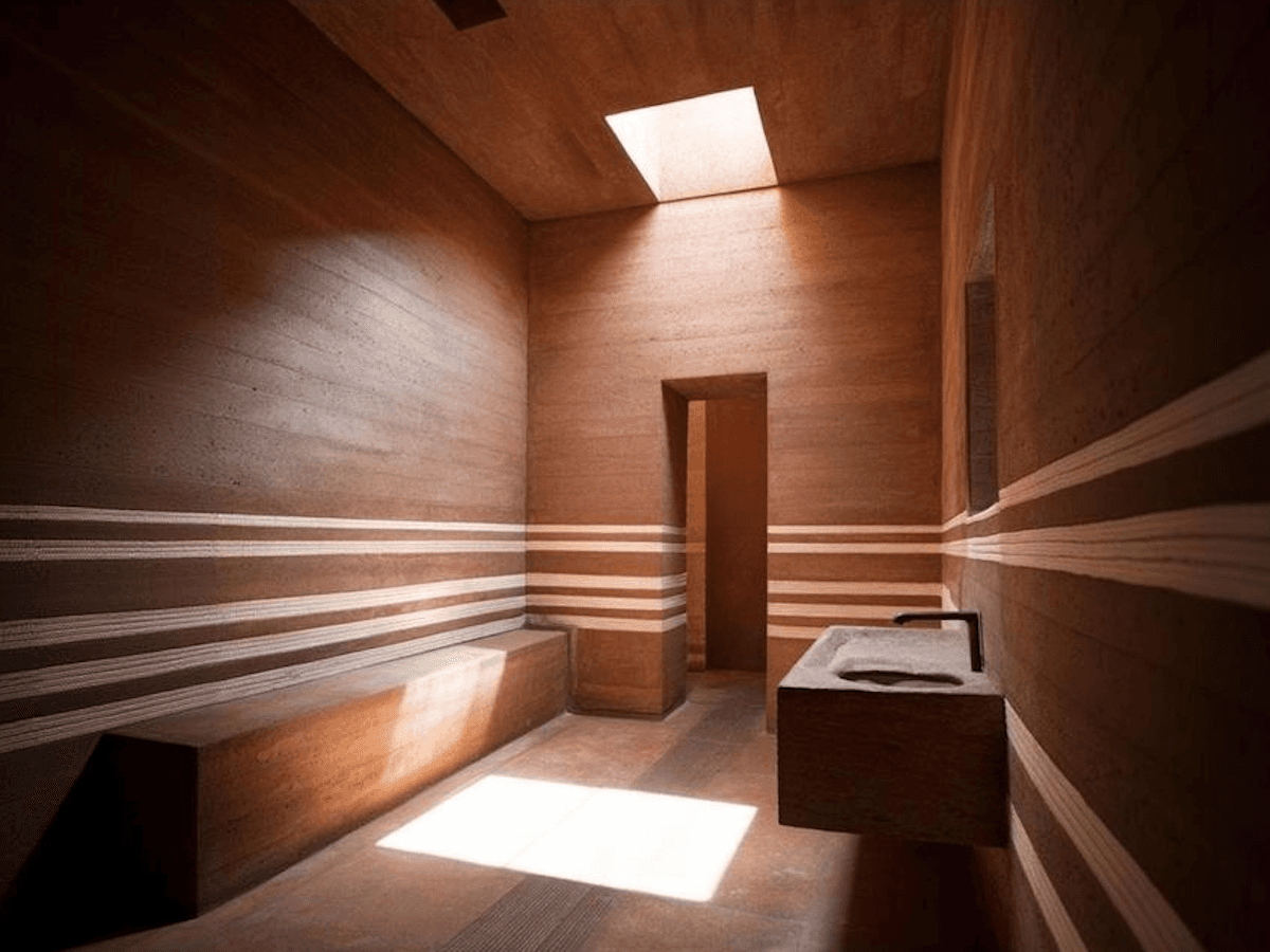 Warm-toned corridor with terracotta walls, horizontal light and shadow striping, curved architectural details, and doorway leading to adjacent room