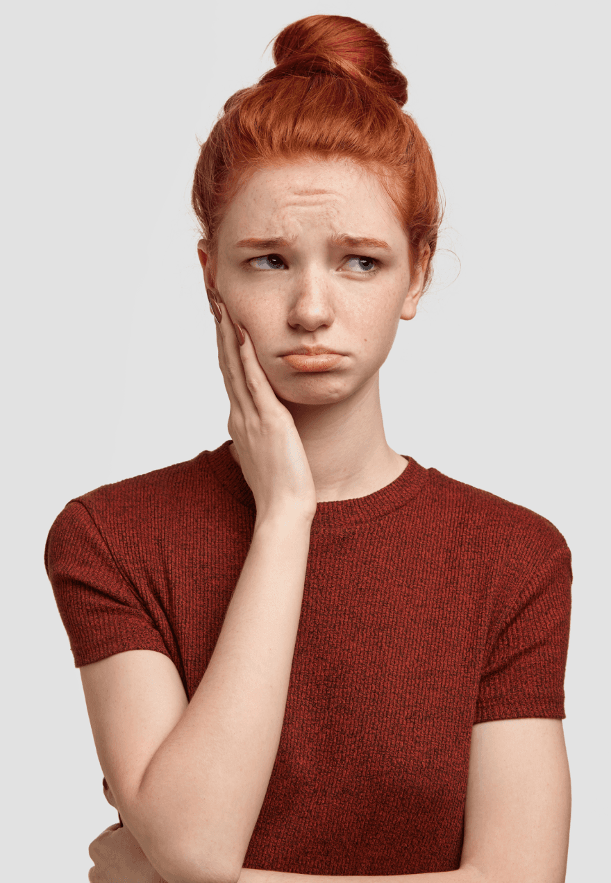 A woman with red hair holding her cheek and looking distressed, indicating dental pain.