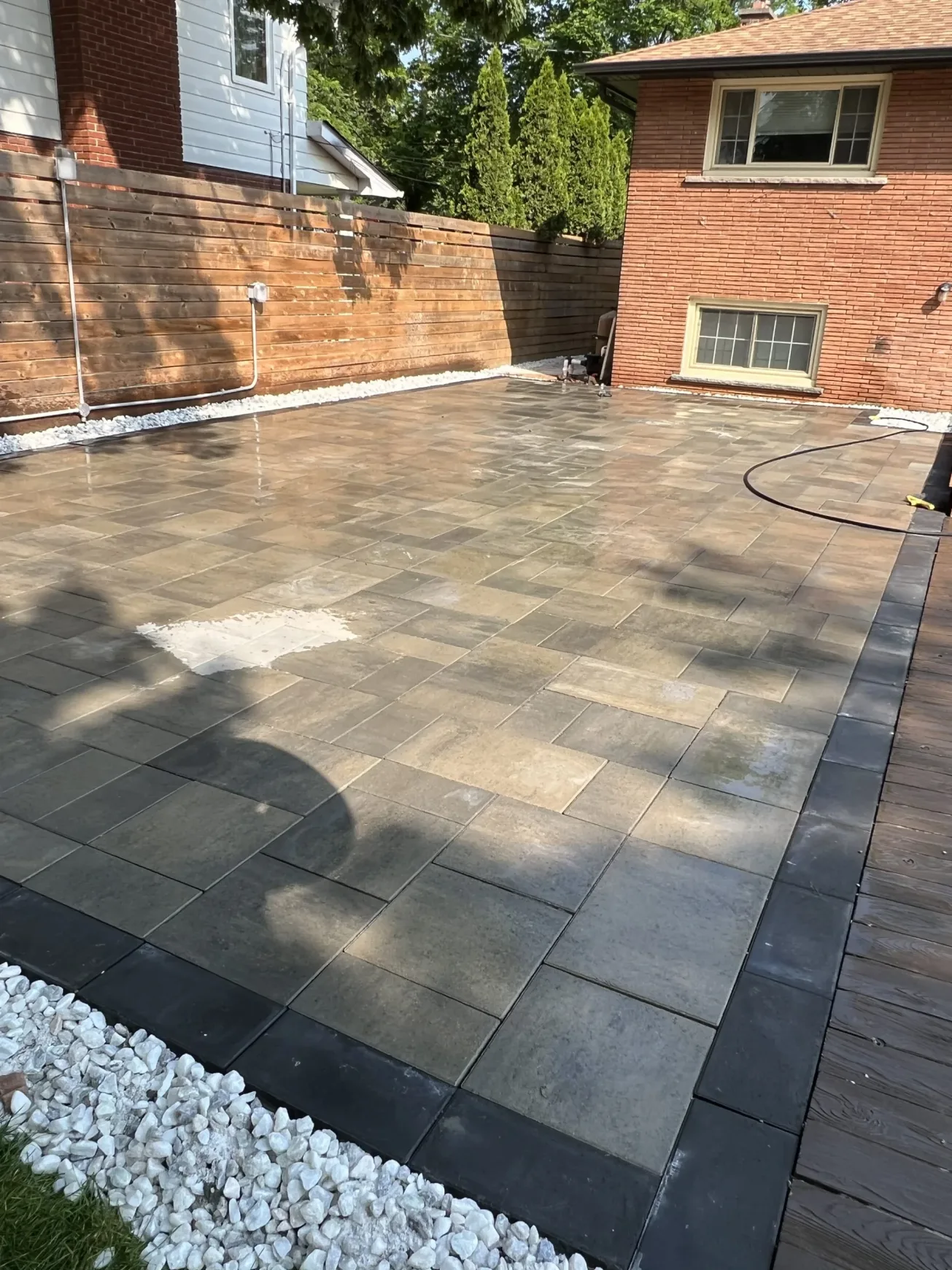 Backyard patio space featuring stone tiles, clean borders, and privacy fencing for a structured landscape look.