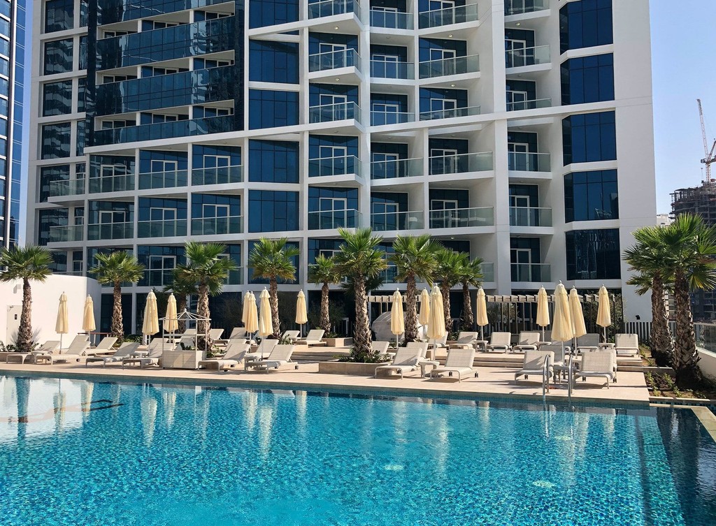Front view of Damac Maison Prive, a stylish hotel with glass facades, set against a backdrop of the waterfront.