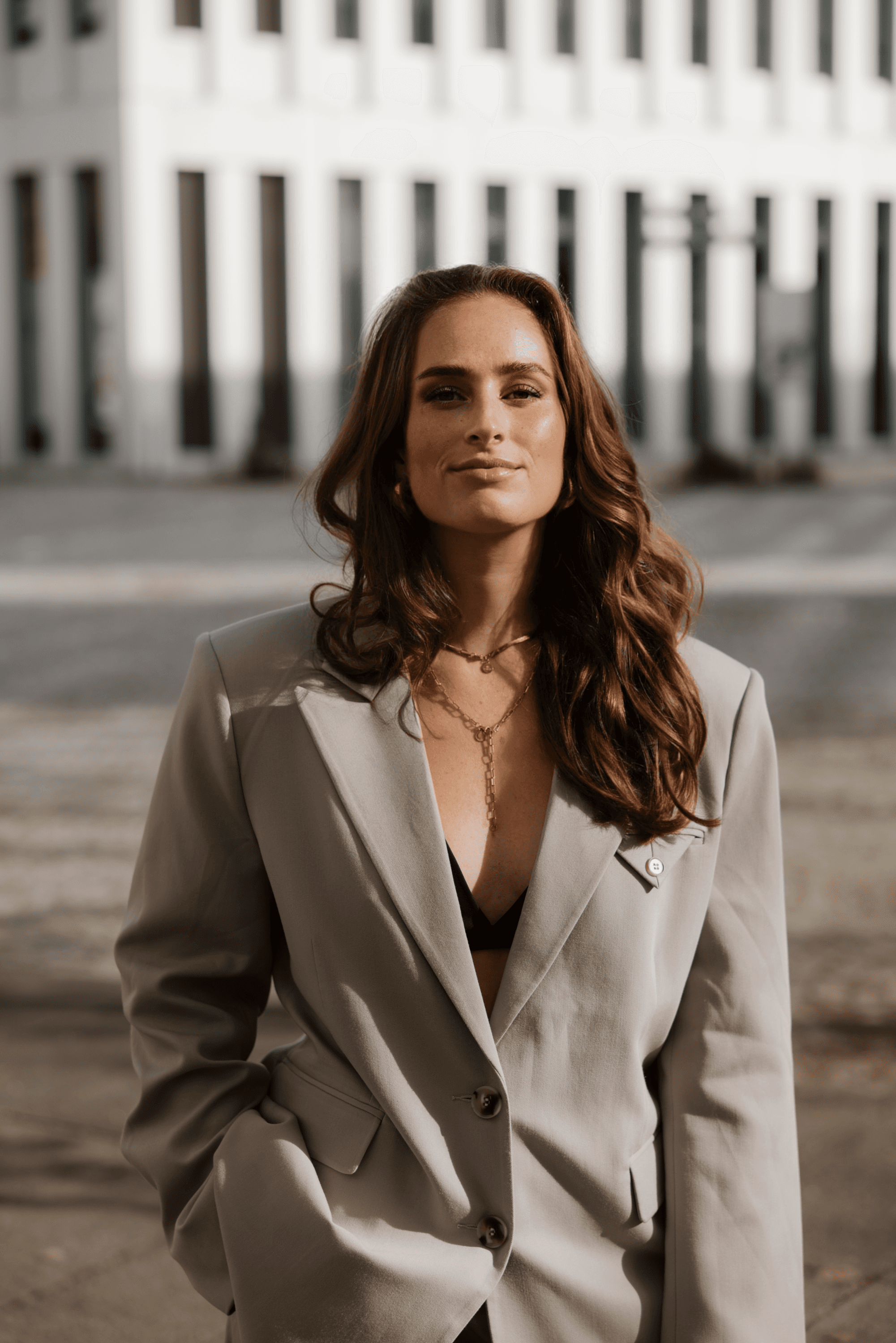 Man with short hair and beard wearing a dark blazer and black shirt against a plain background.