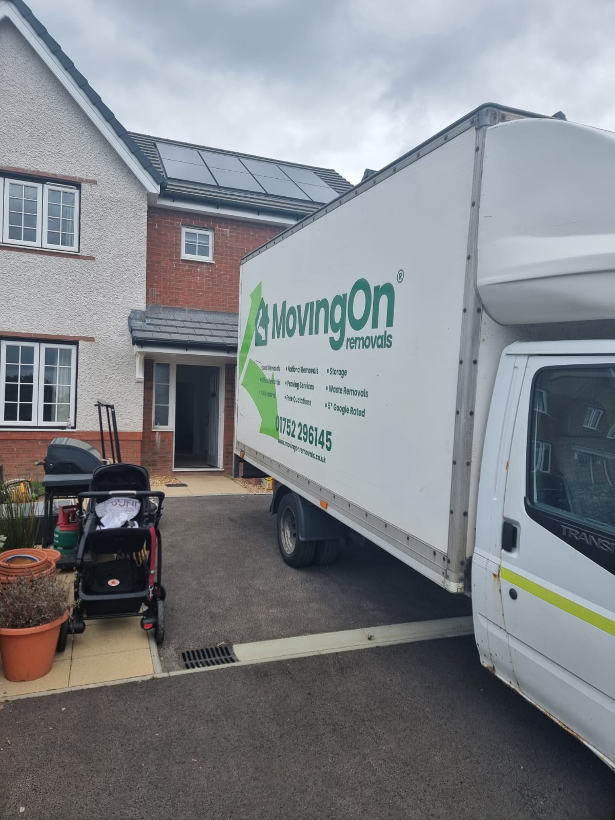 A professional MovingOn Removals Luton van parked in a residential driveway in front of a modern house, with moving equipment and a stroller in the foreground, ready for a family home relocation.