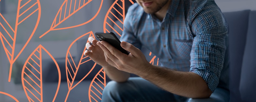 Man sitting on a couch and playing with his phone, likely engaging with an Alumni app