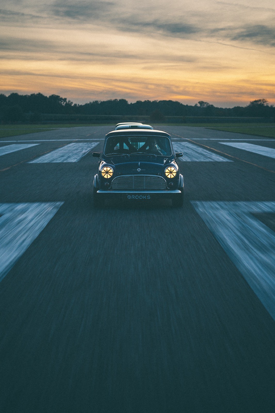 A small, green and black vehicle parked on a sandy surface, with a warm sunset lighting the scene.