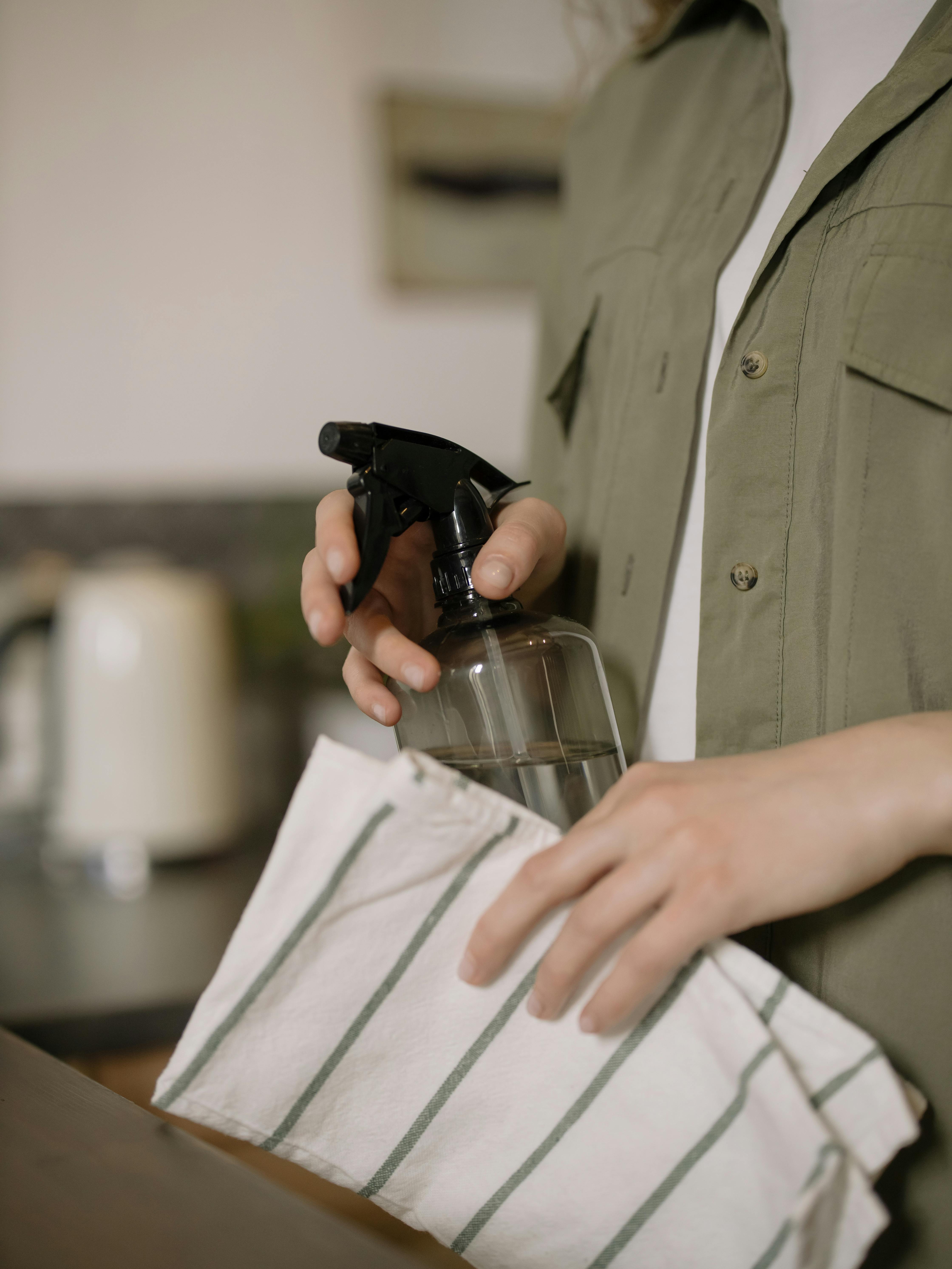 Person holding spray bottle and striped cloth for cleaning