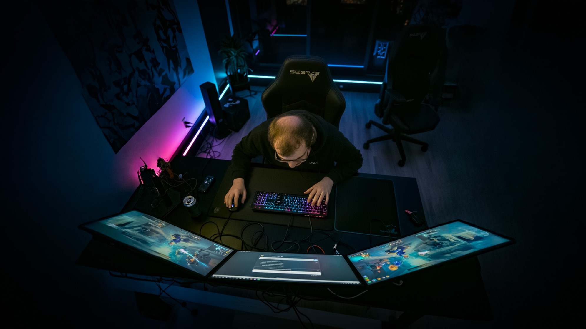 Overhead shot of a gamer in a dark room surrounded by multiple monitors and LED lights. Represents the isolation and digital lifestyle of the target audience, establishing the context for a relatable patient story in the gaming community.