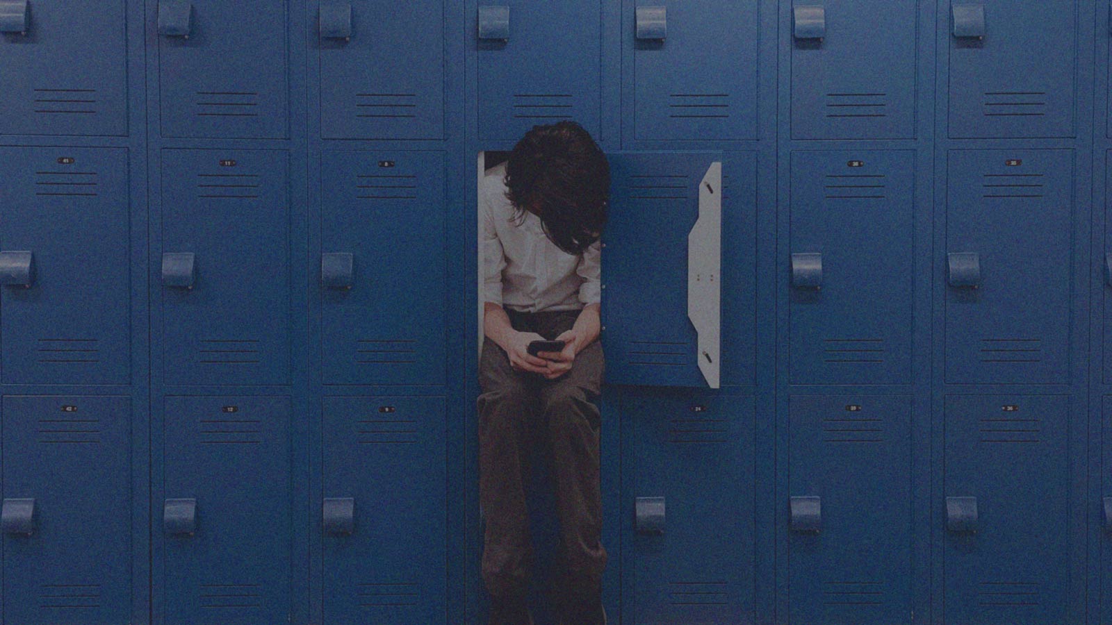 Foto que muestra a un niño solo que está sentado en un locker con un celular en sus manos, en la columna de opinión Para sus hijos, Montessori; para los ajenos, el algoritmo de IdeaPaís.