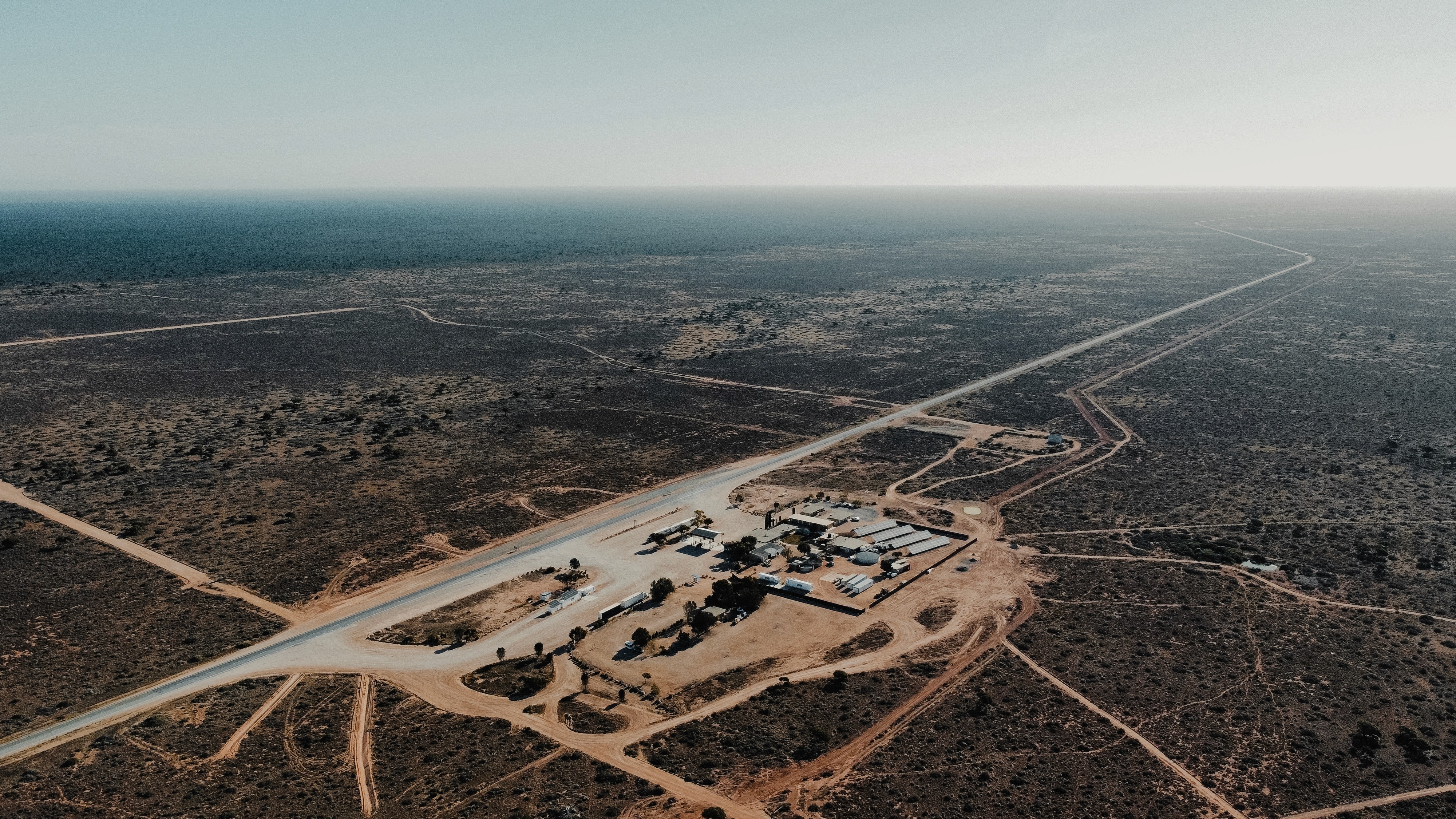 Aerial view of a remote industrial facility in the Pilbara region of Western Australia with a long highway and network of dirt tracks.