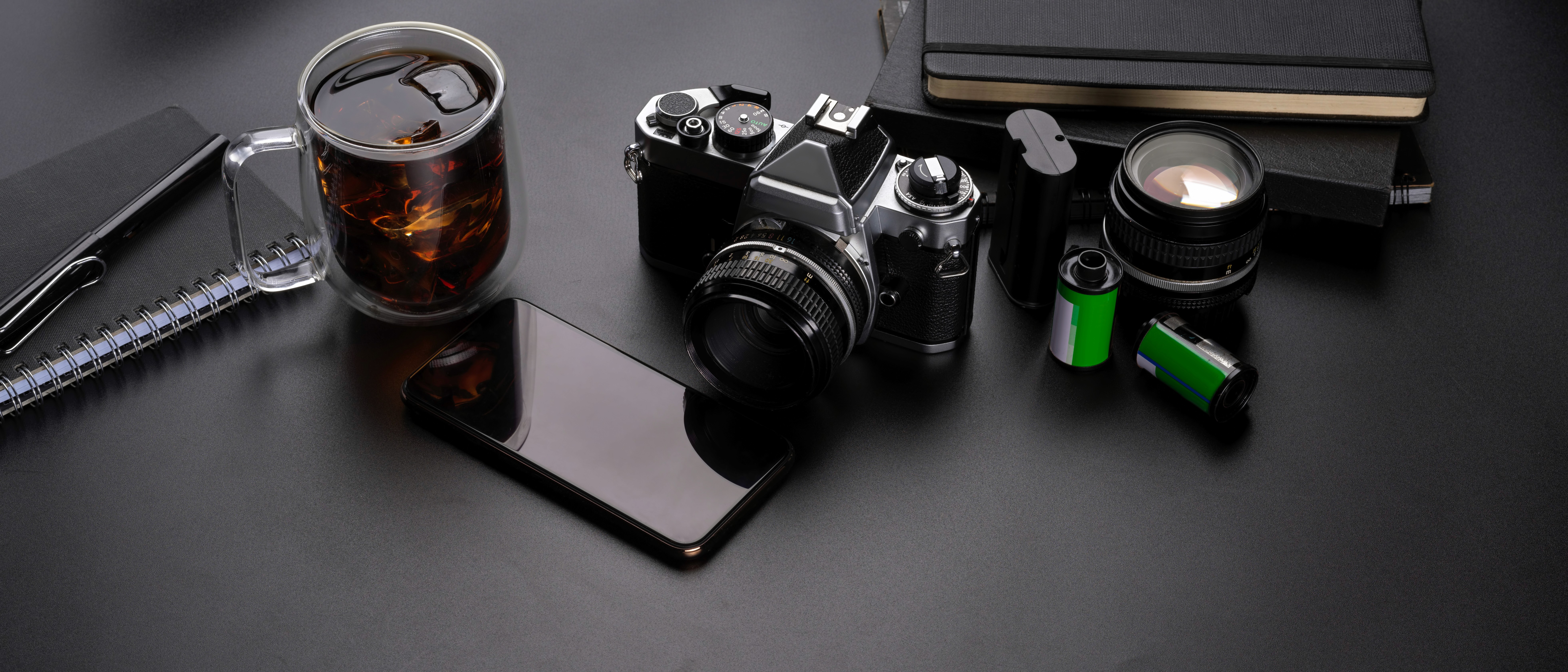 Black and white flat lay of a camera, sunglasses, notebook, and a glass of tea.