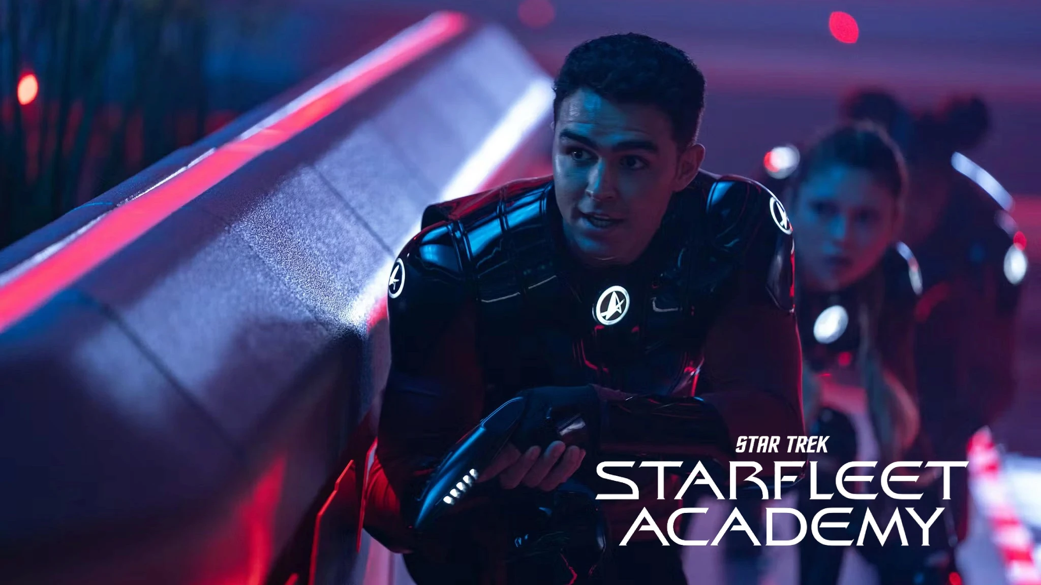 A young person in futuristic black futuristic armour crouches with a focused expression, holding a high-tech device, against the backdrop of a sleek, dimly-lit corridor, accompanied by the text "Star Trek Starfleet Academy."