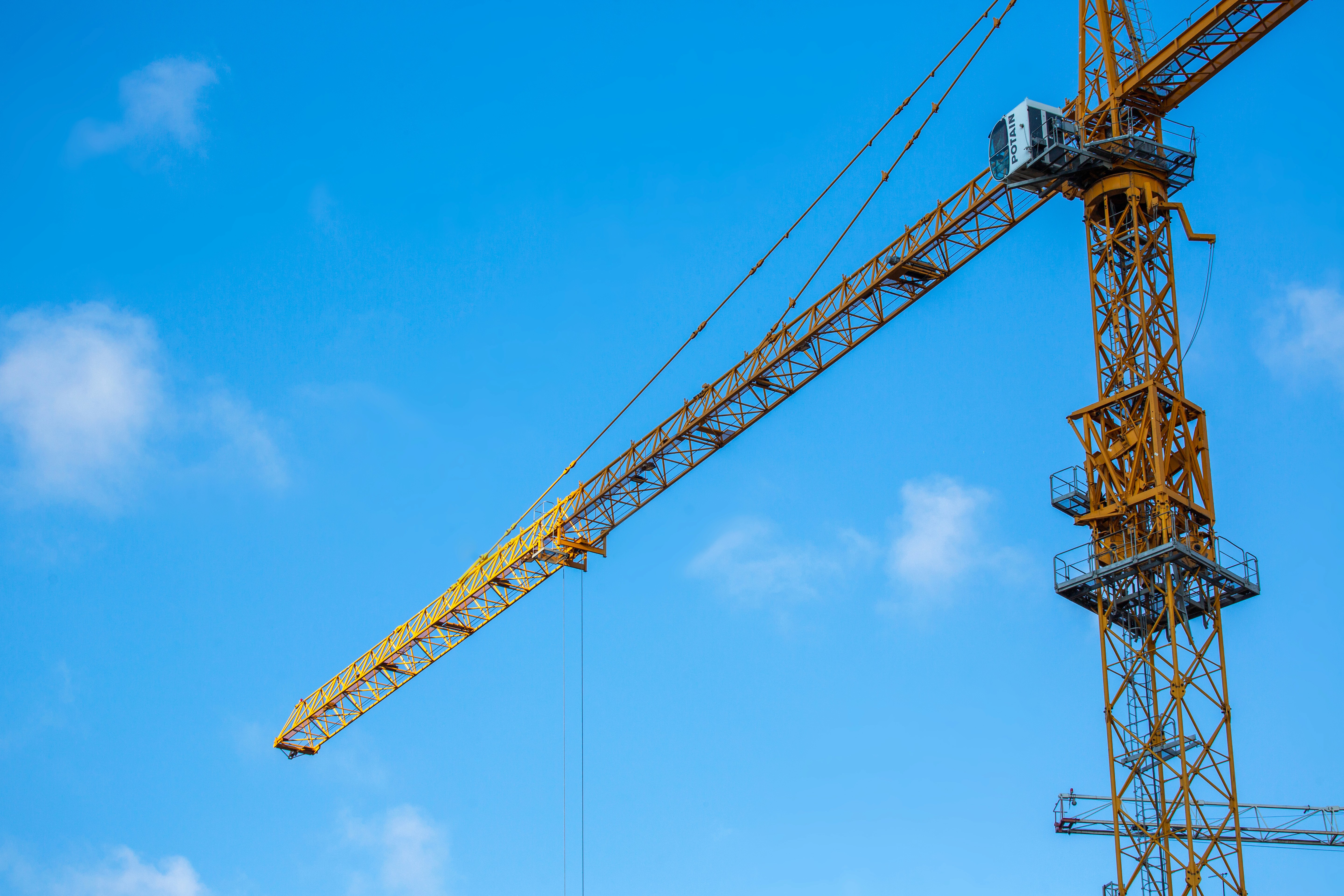 A large yellow construction crane extends across a bright blue sky with scattered clouds, conveying a sense of industrial progress and development.