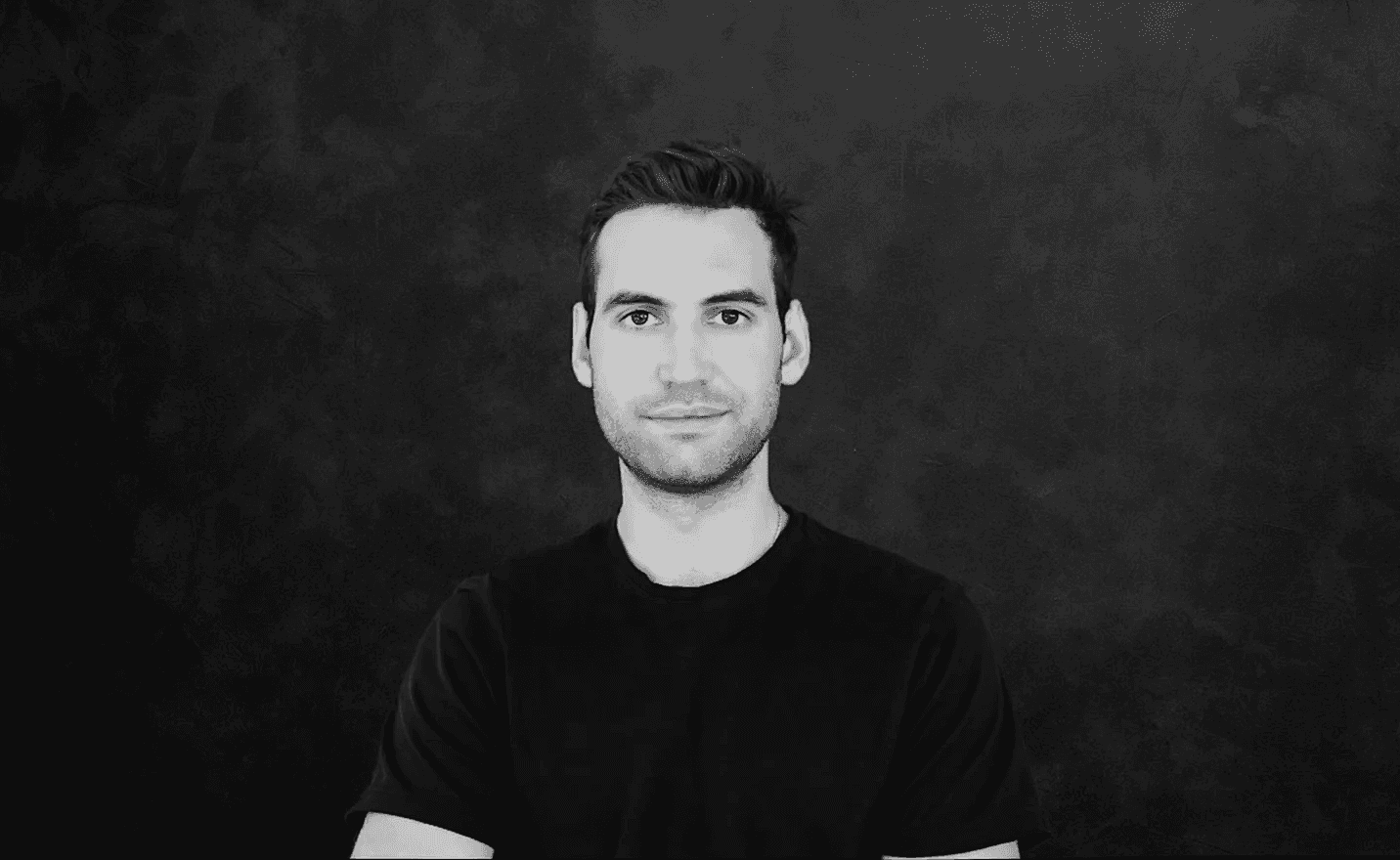 Portrait of a woman with long, smooth hair swept to the side, in a dark t-shirt, on a plain background.