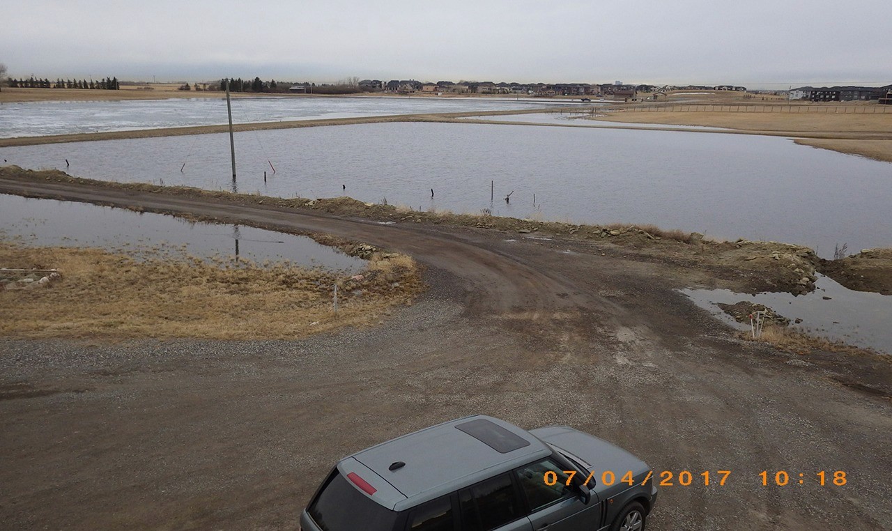 Flooded rural access road and agricultural land near residential developmen