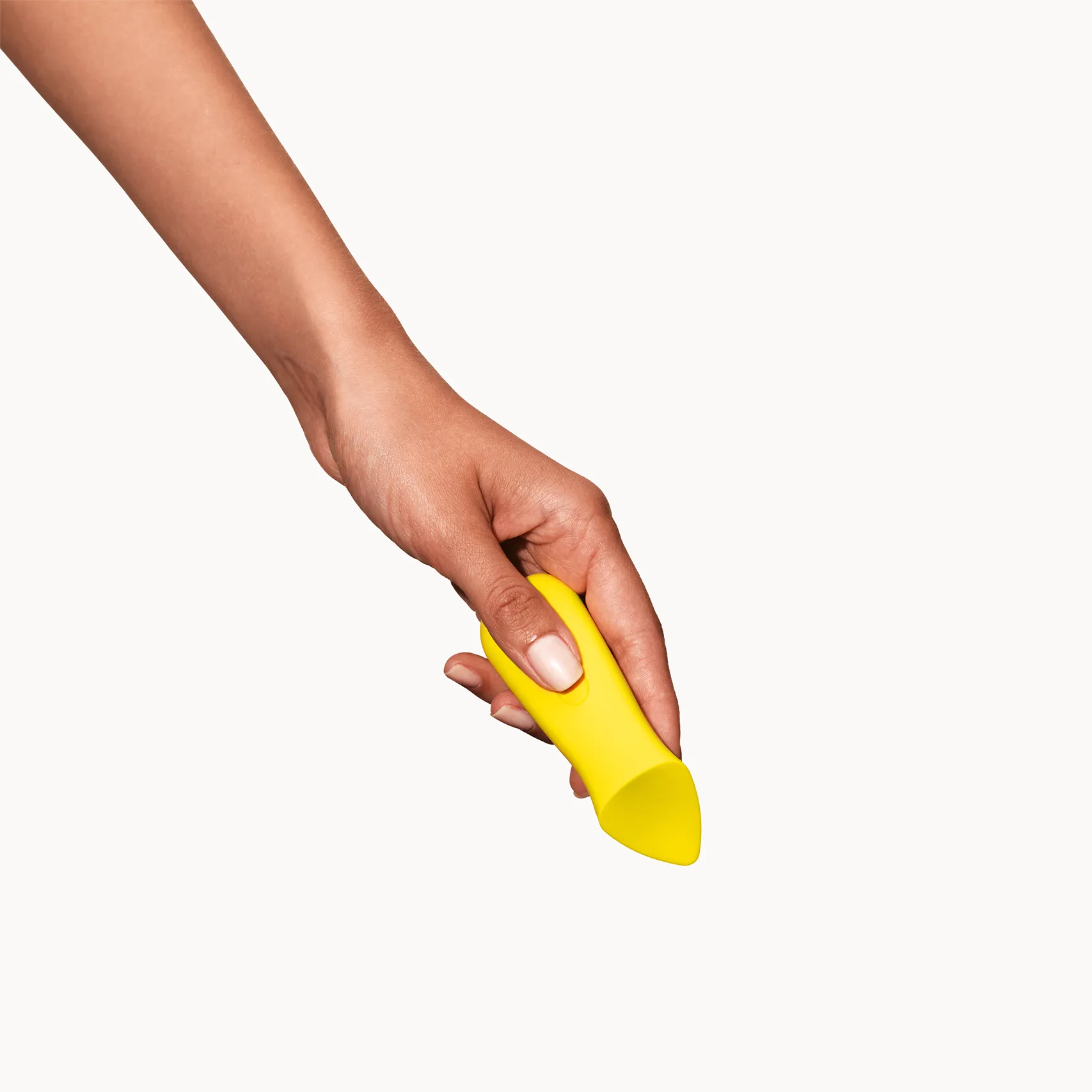 Hand holding a yellow Kip ergonomic sexual wellness device on a white background